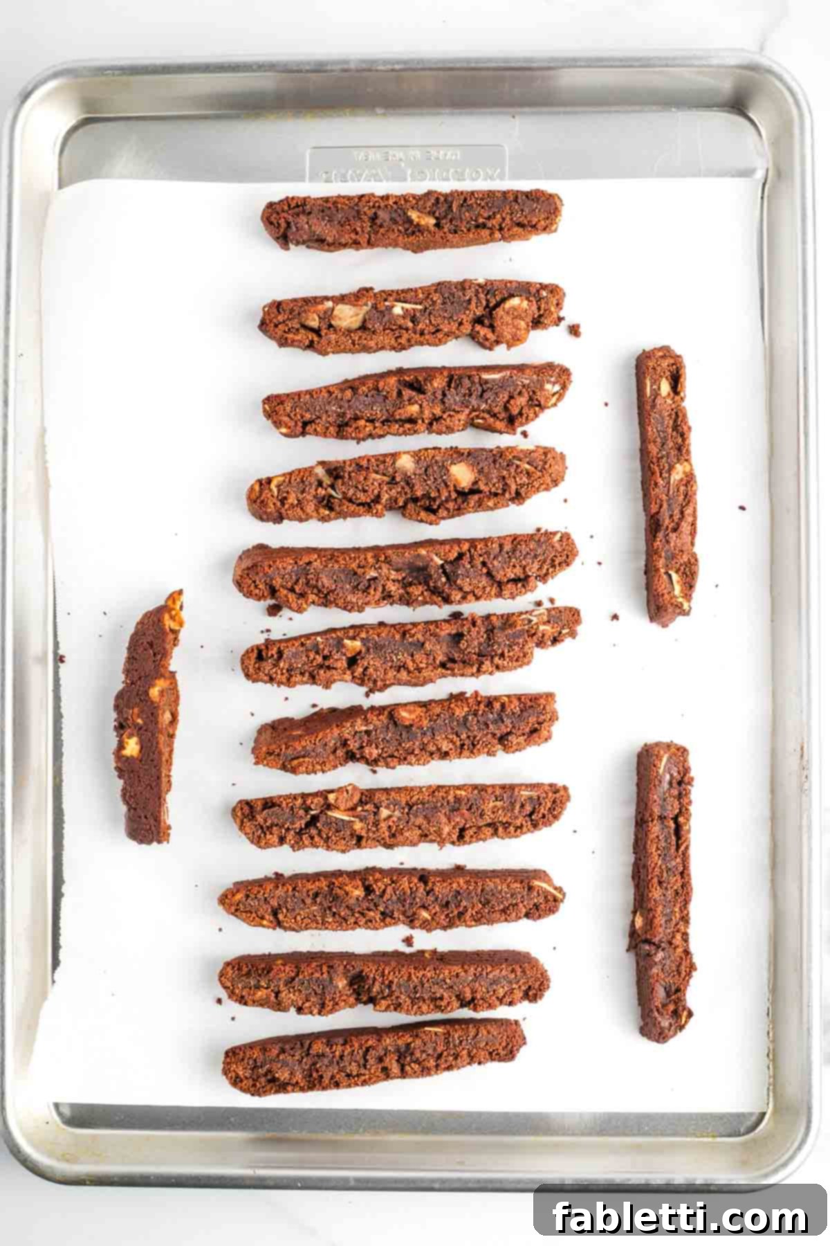 Irresistible Vegan Gluten-Free Chocolate Almond Biscotti 14 Sliced chocolate biscotti arranged on their sides on a baking sheet.