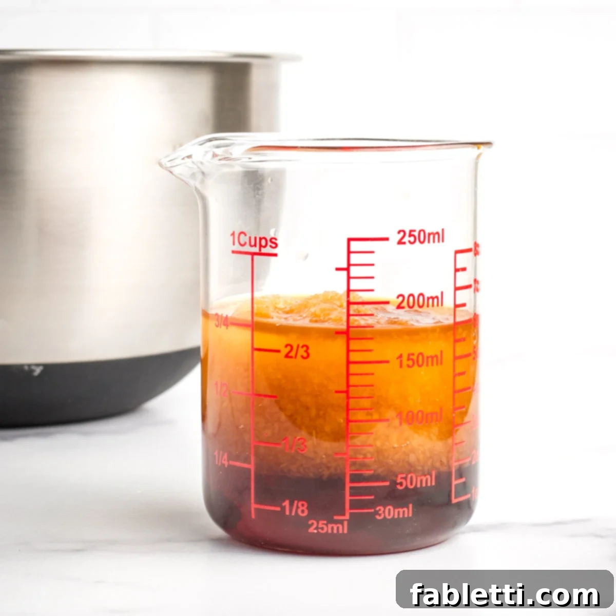 Irresistible Vegan Gluten-Free Chocolate Almond Biscotti 5 Glass measuring cup showing darker liquid on the bottom and cloudy above it, with a mixing bowl in the background.