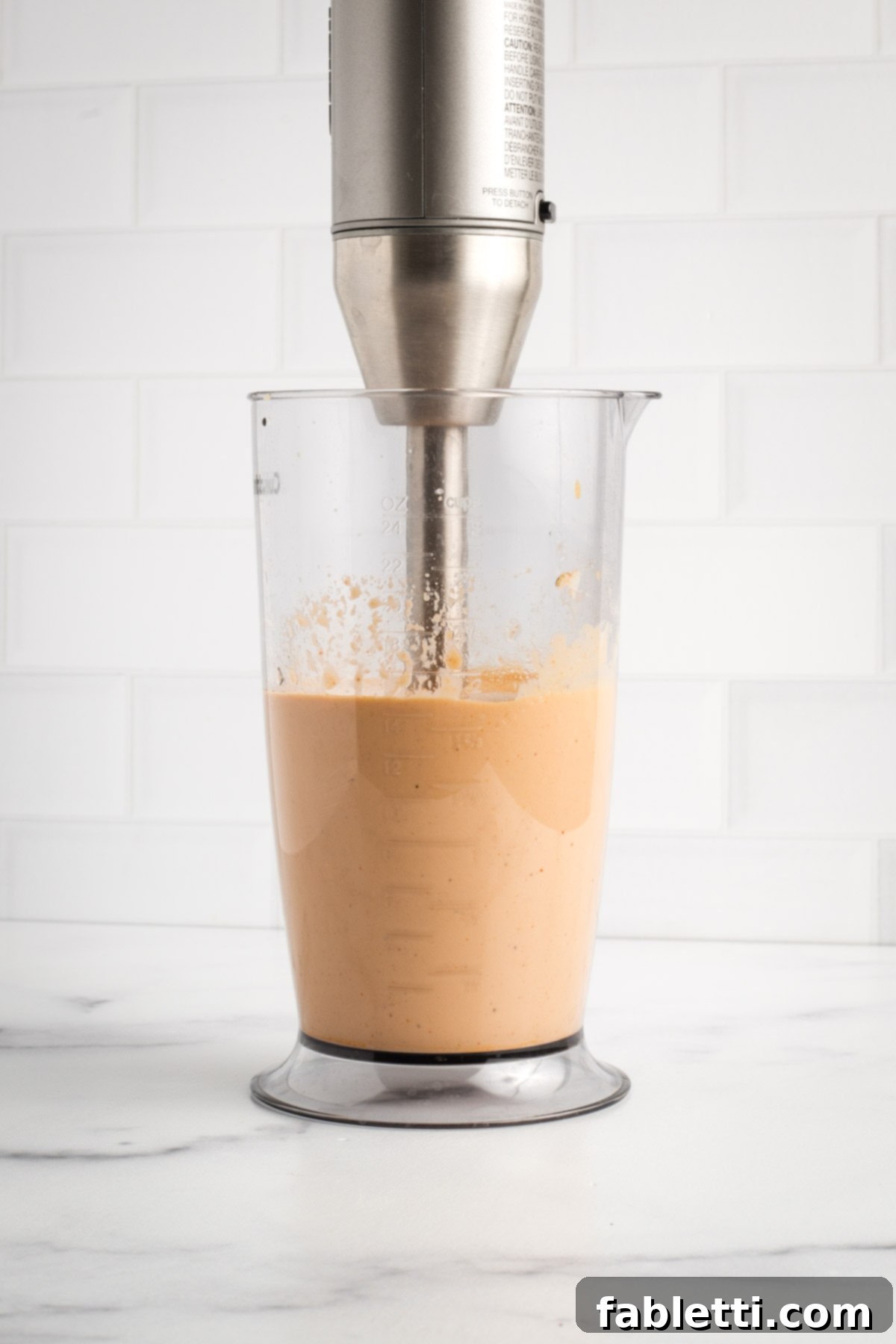 Creamy Tofu Vegan Big Mac Sauce 5 Immersion blender pureeing some peach colored sauce in a tall container.