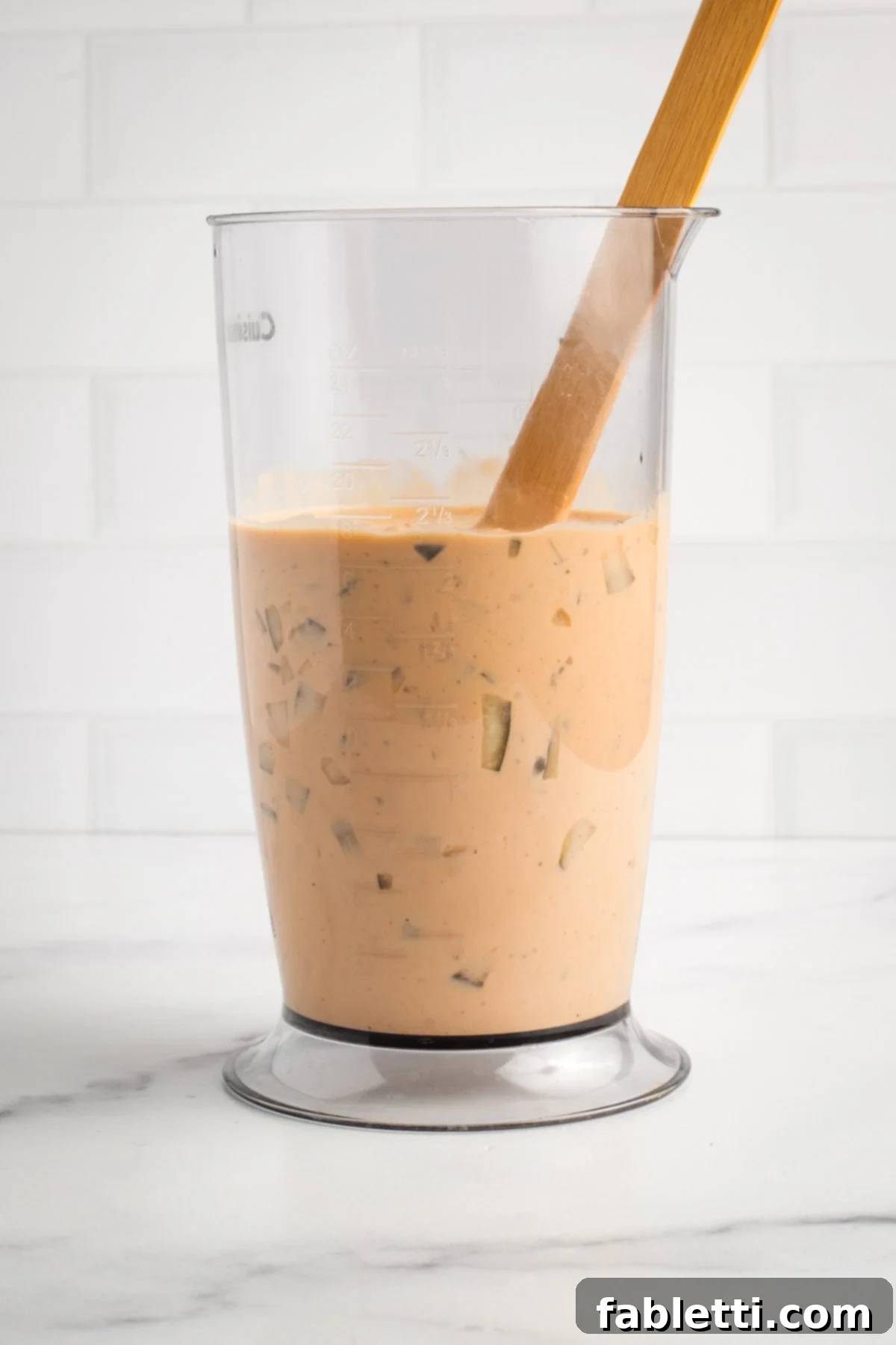 Creamy Tofu Vegan Big Mac Sauce 9 Stirring diced pickles into a container of peach colored burger sauce.