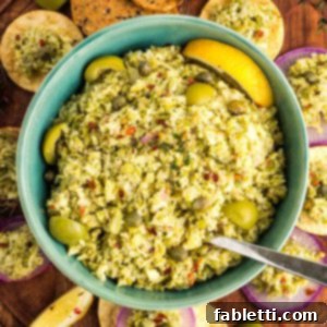 Bowl of green olive tapenade with capers and lemon, surrounded by crackers and radish slices with the olive spread.