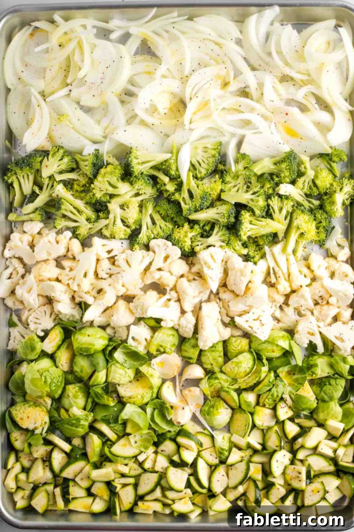 Sheet Pan Green Velvet Soup 5 Rows of chopped veggies on a sheet pan. Onion, zucchini, cauliflower, brussels sprouts and some cloves of garlic with the skins still on.