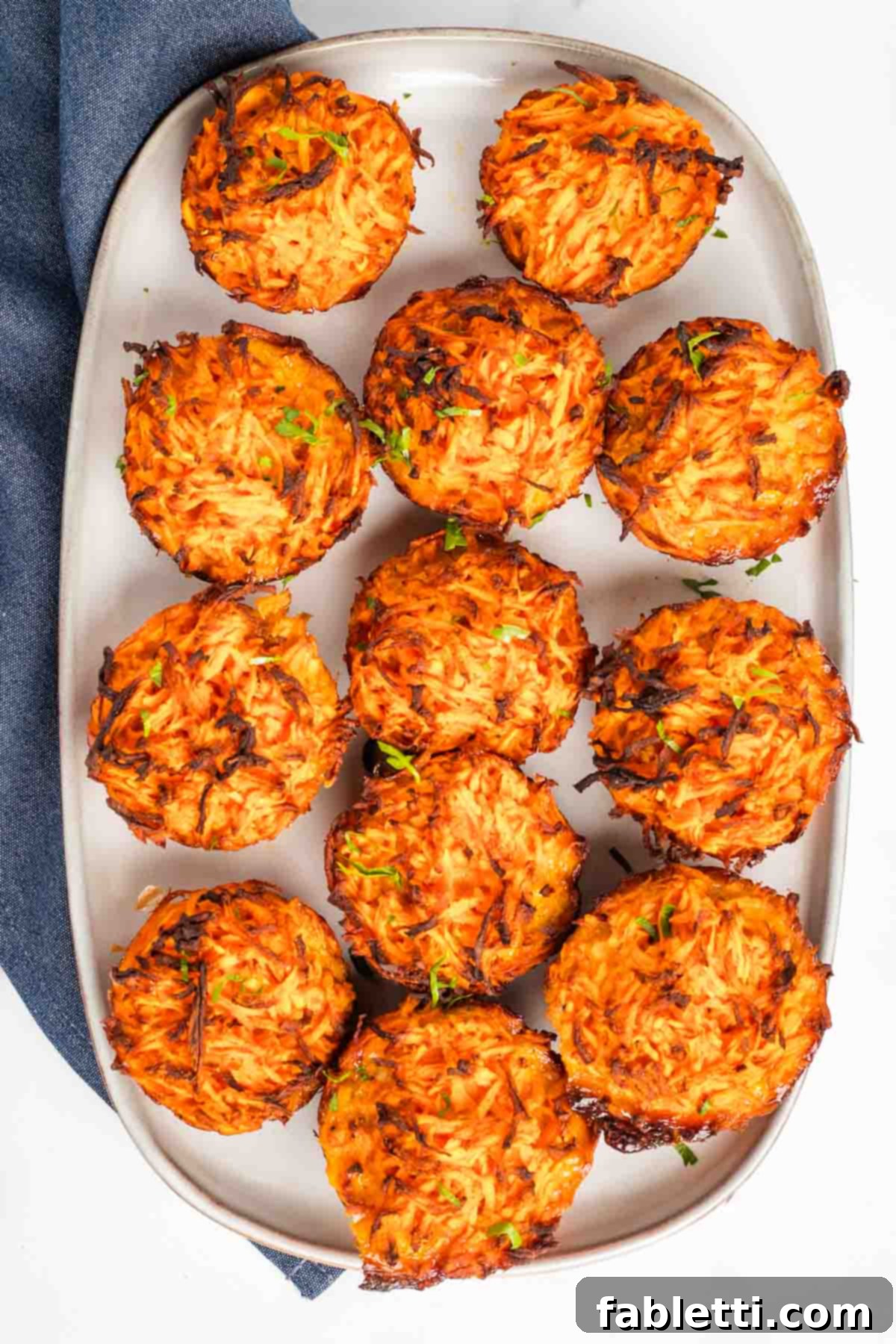Golden Sweet Potato Kugel Cups 2 Crispy sweet potato kugel muffins on a plate, sprinkled with fresh herbs.