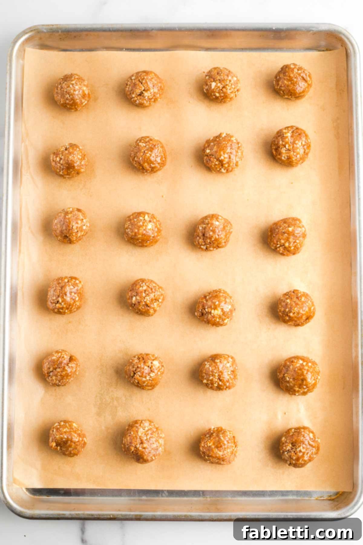 Decadent Vegan Chocolate Almond Macarons 12 Almond cookies, rolled into balls, arranged on a parchment-lined baking tray.