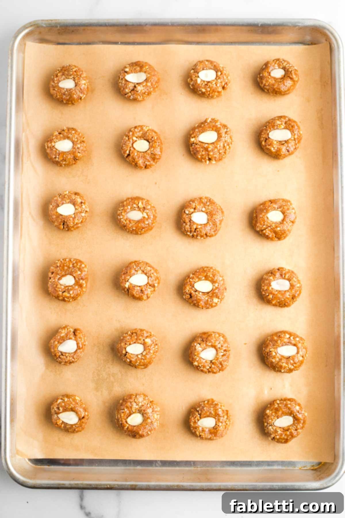 Decadent Vegan Chocolate Almond Macarons 13 Almond cookies with a decorative almond slice in the center, lined up on a baking sheet, ready to bake.