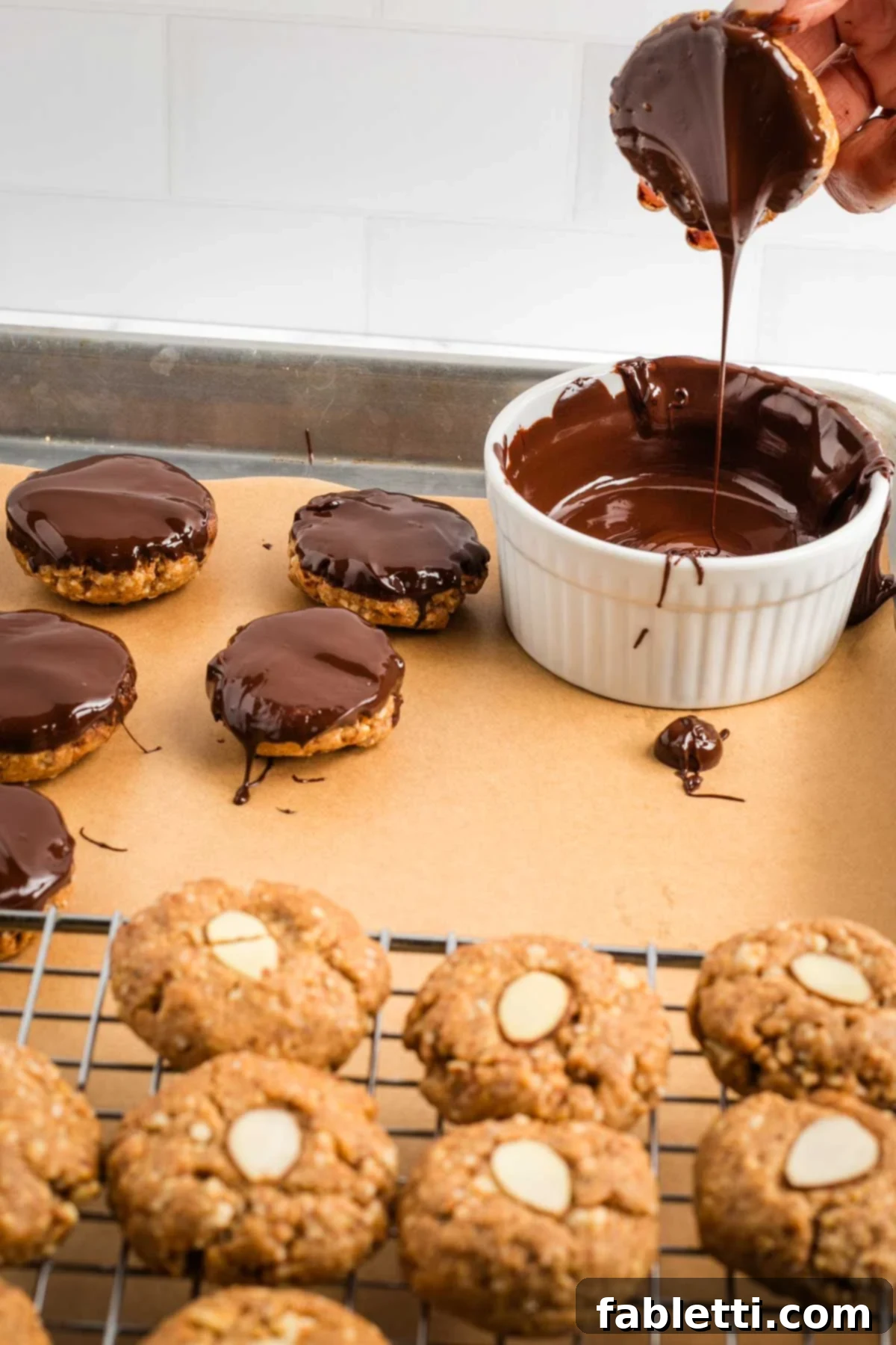 Decadent Vegan Chocolate Almond Macarons 17 A chocolate-dipped almond macaroon, upside down on parchment paper, allowing excess chocolate to drip off.