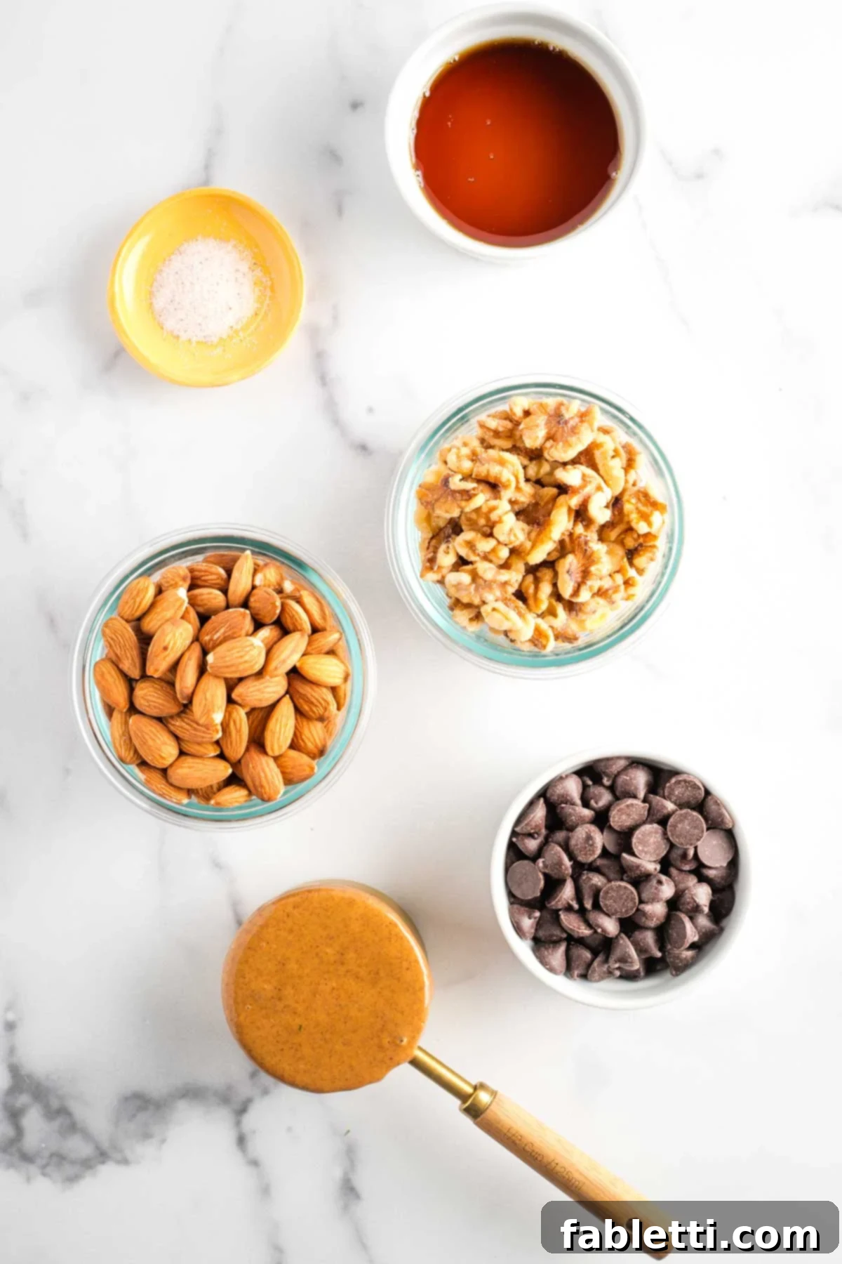 Decadent Vegan Chocolate Almond Macarons 3 Small bowls displaying maple syrup, sea salt, whole almonds, walnuts, almond butter, and dark chocolate chips.
