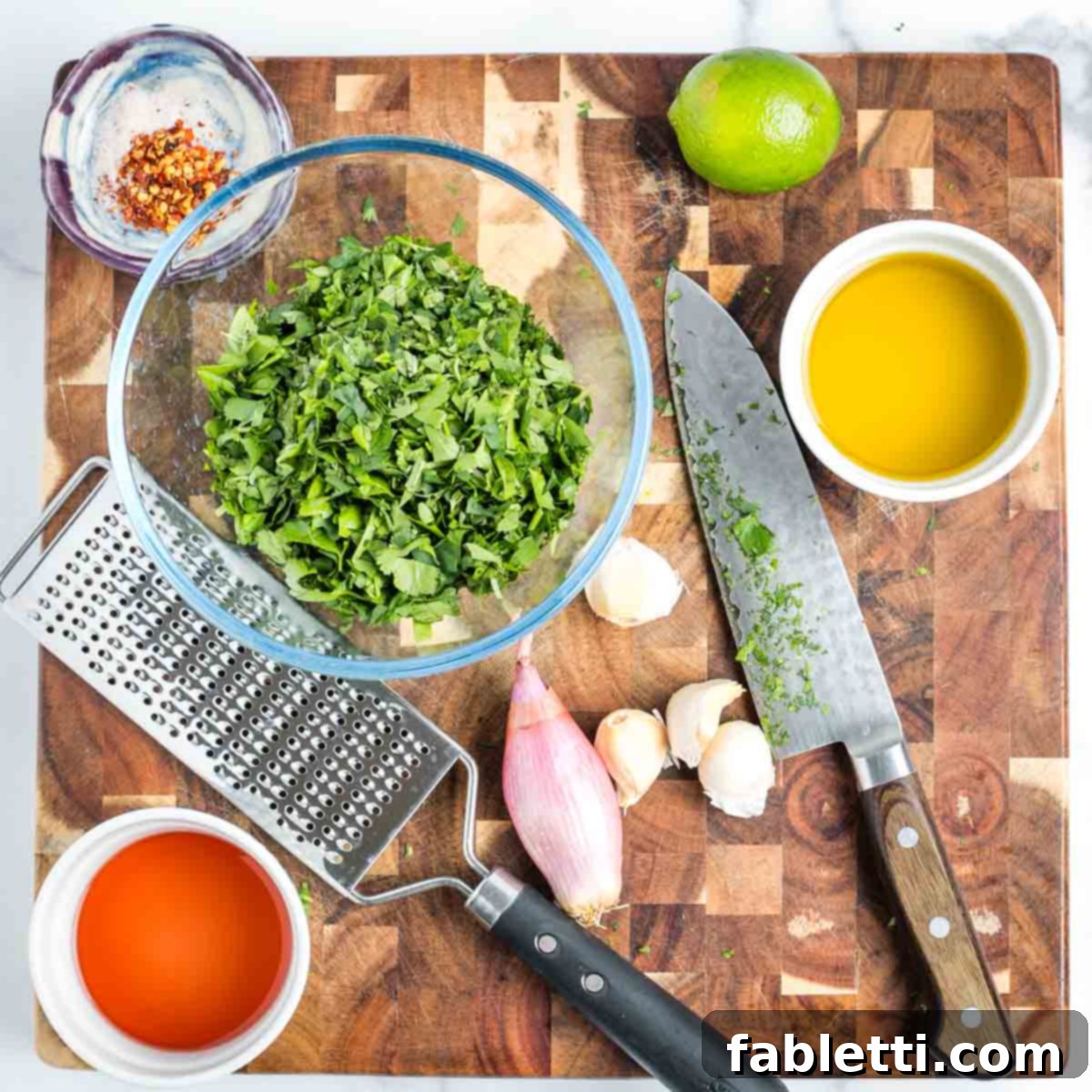Zesty Chimichurri Portobello Steaks 10 Cutting board filled with chimichurri ingredients, including bowl of finely chopped fresh herbs, garlic cloves, a lime, salt and pepper, a dish with red wine vinegar and some olive oil.
