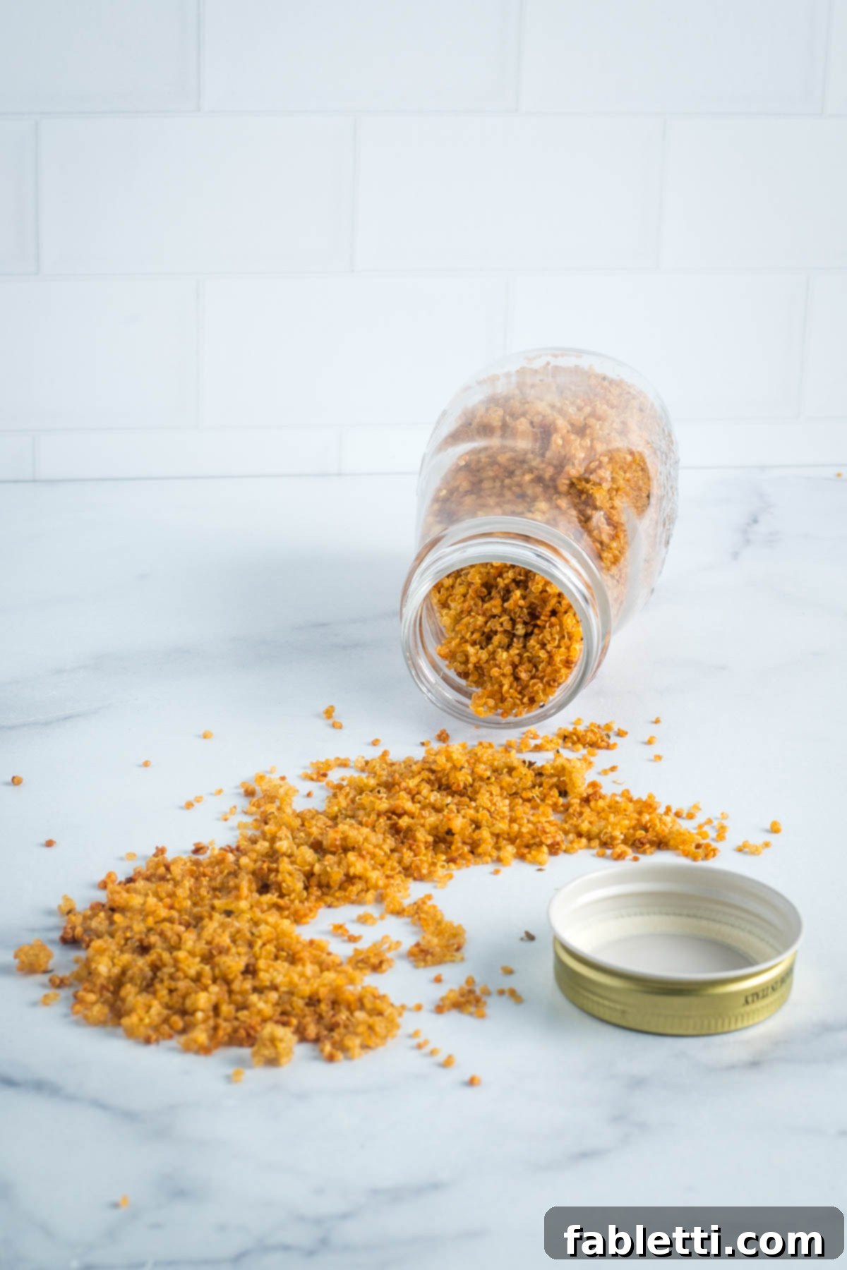 Jar of crispy quinoa spilling out onto the countertop, showcasing its golden, crunchy texture.