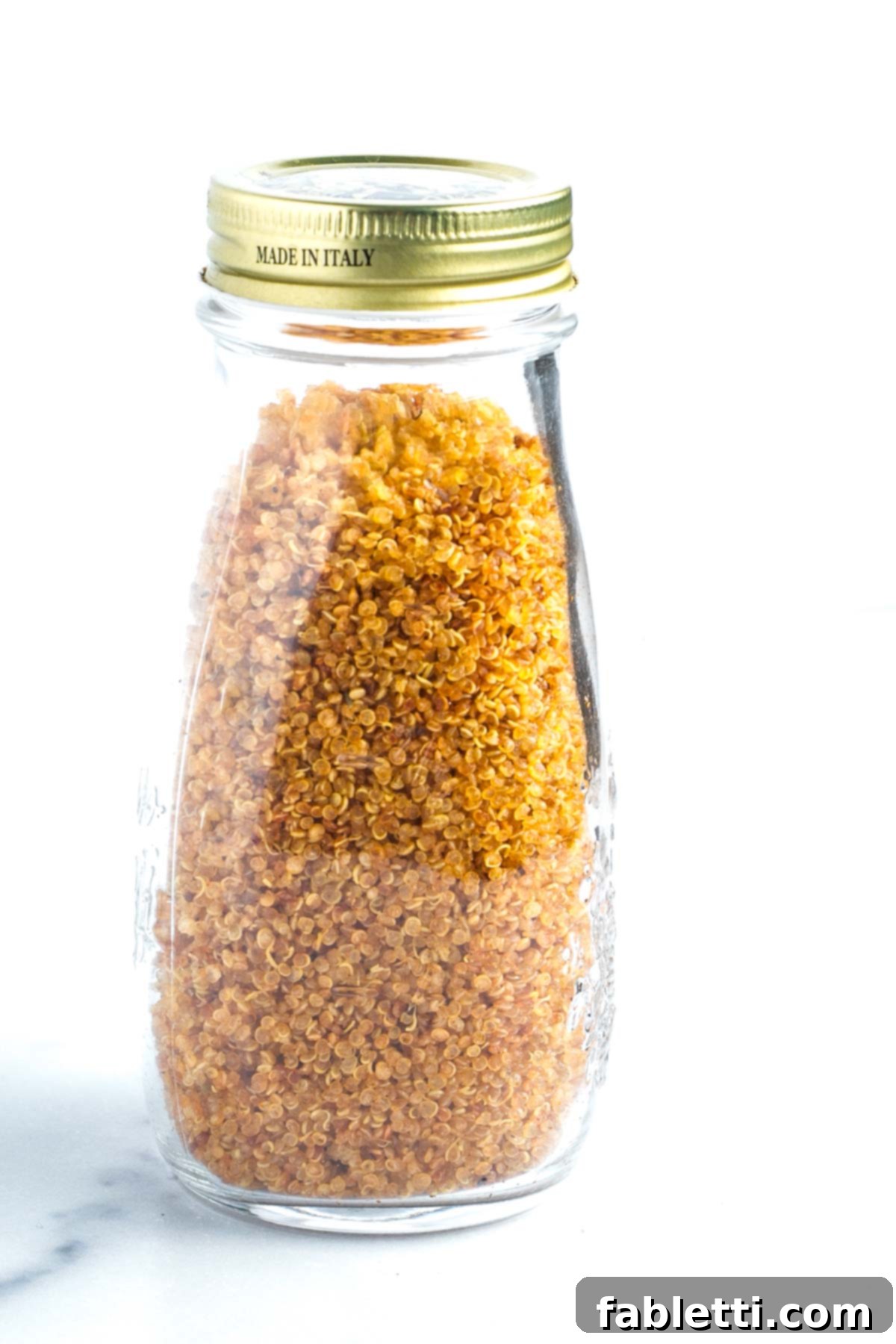 A stylish glass bottle filled to the brim with perfectly golden, crispy quinoa, ready for use.