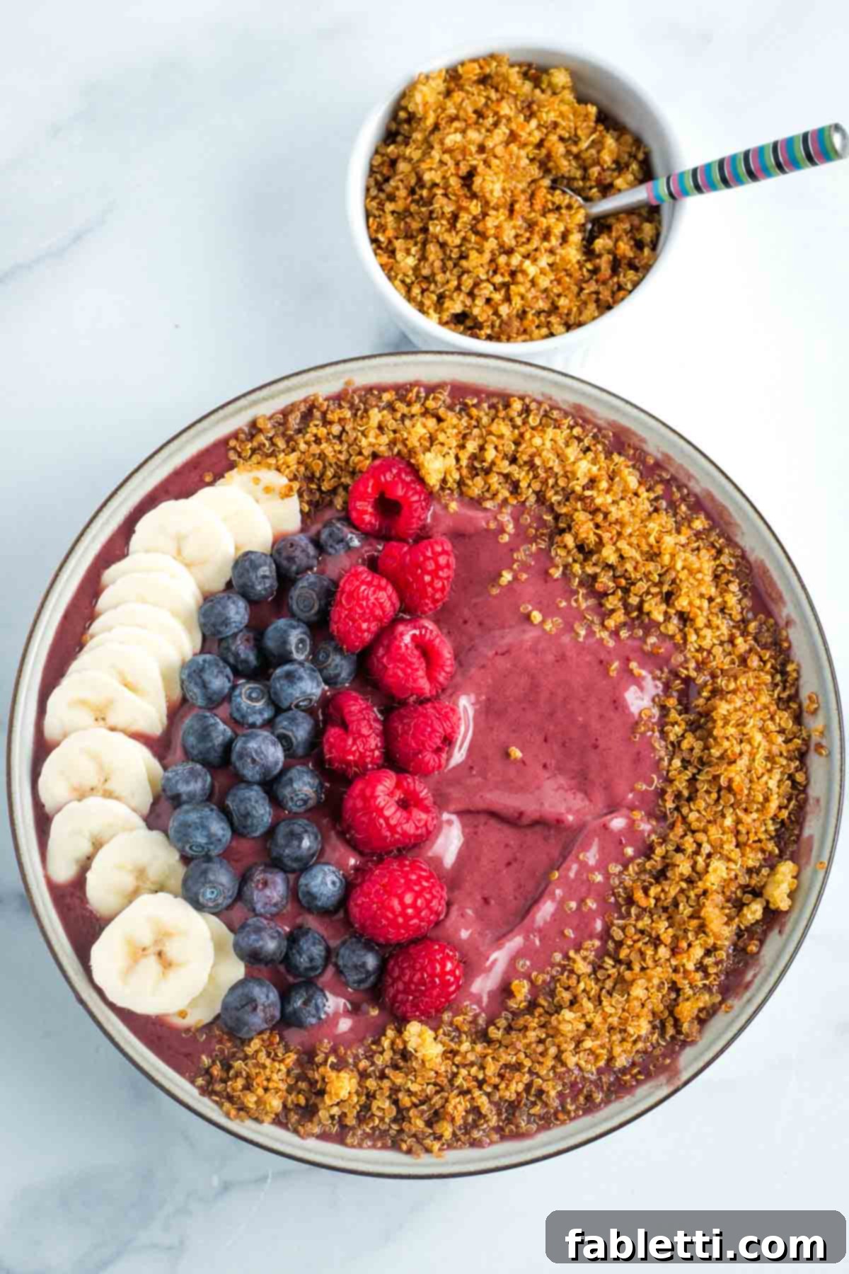 A vibrant, deep purple frozen smoothie bowl, artfully topped with fresh berries, banana slices, and a generous sprinkle of sweet crispy quinoa.