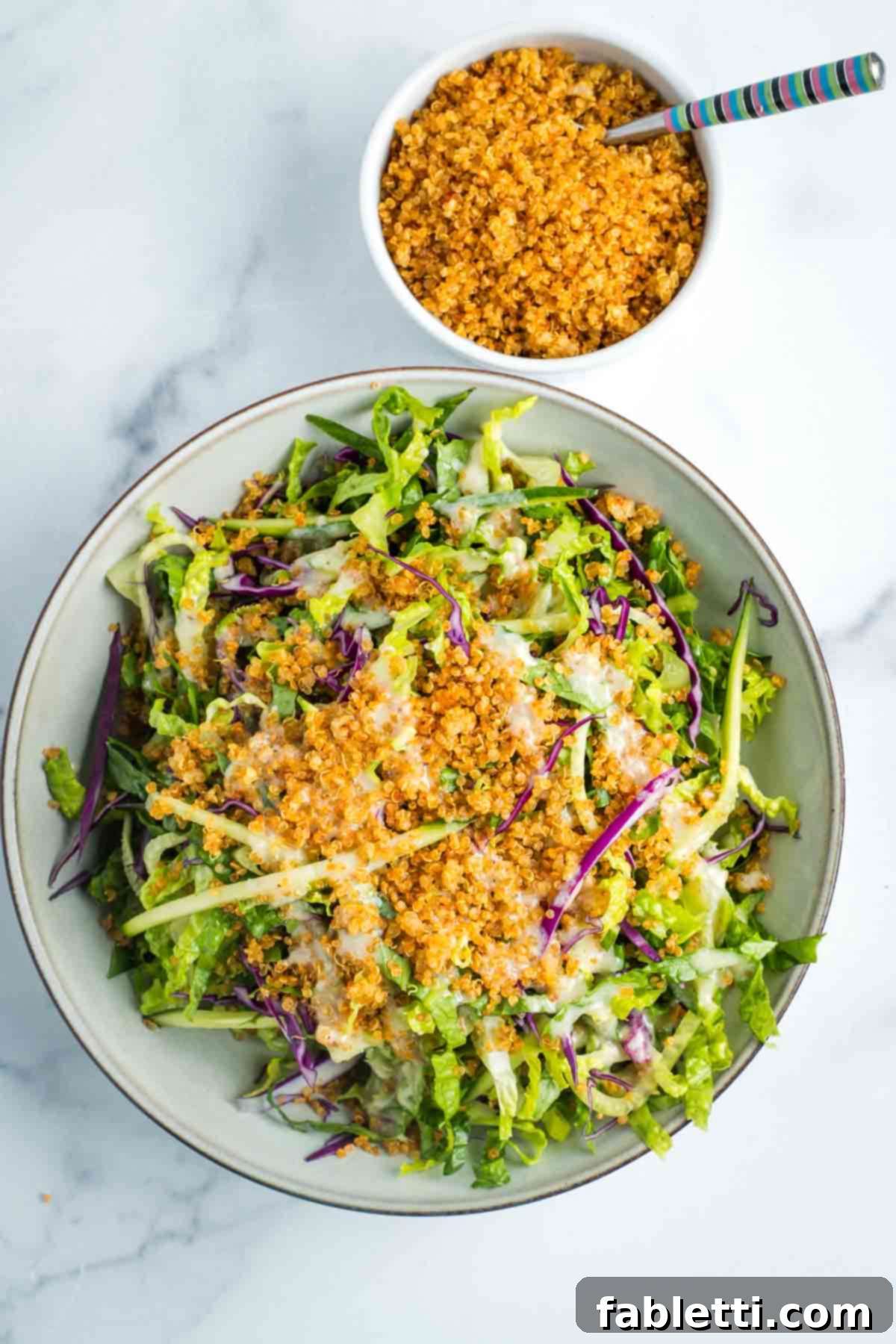 A fresh, simple salad generously topped with golden, savory crispy quinoa and a drizzle of creamy Caesar dressing.