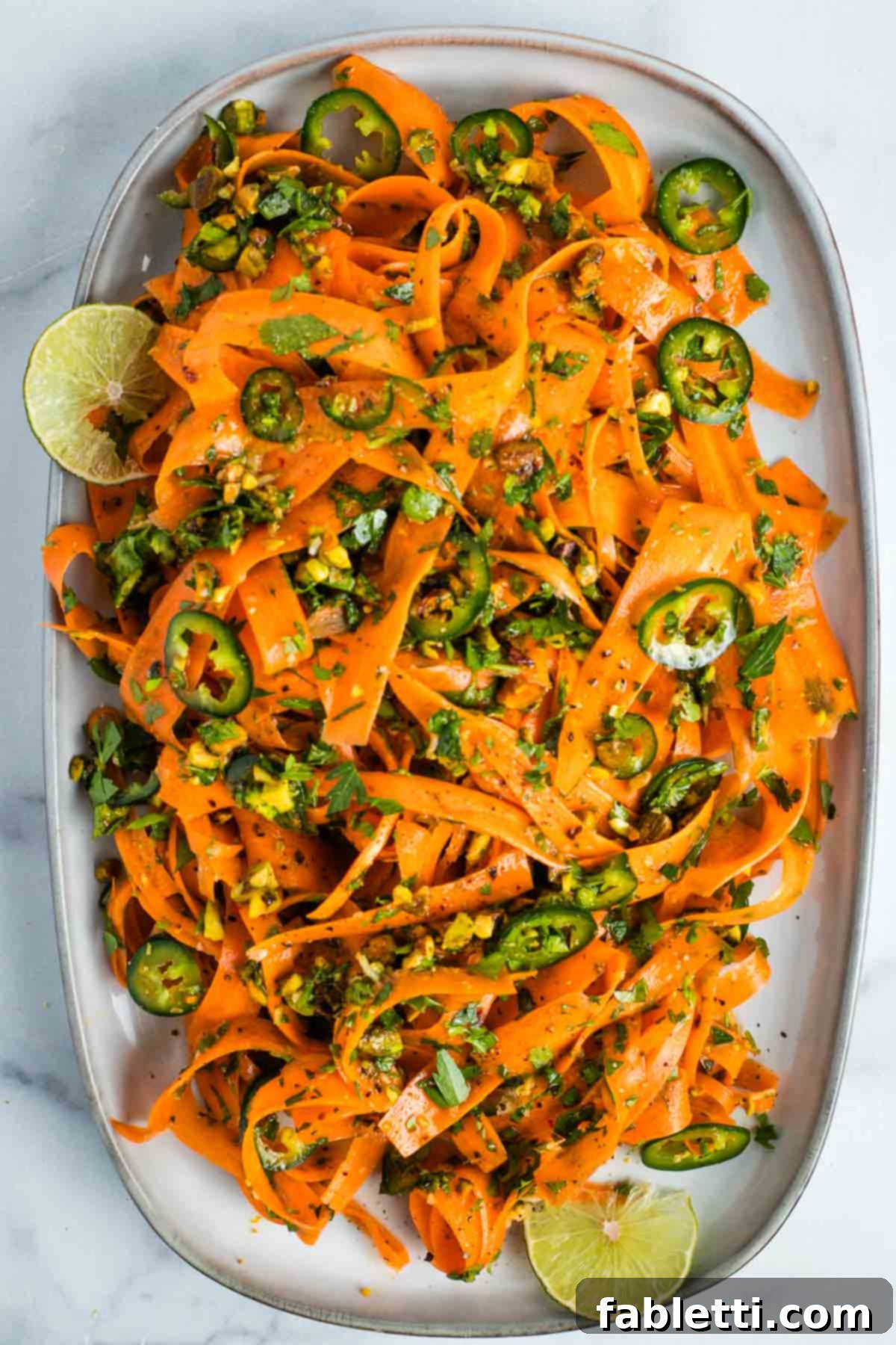 Sweet Heat Shaved Carrot Salad 2 Vibrant carrot ribbons, generously sprinkled with fresh green herbs, chopped pistachios, zesty lime wedges, and thinly sliced red jalapenos, ready to serve.