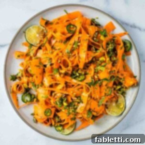 Sweet Heat Shaved Carrot Salad 11 Ribbons of carrots, garnished with sliced jalapenos, chopped parsley, and crunchy pistachios, presented as a vibrant and inviting salad.