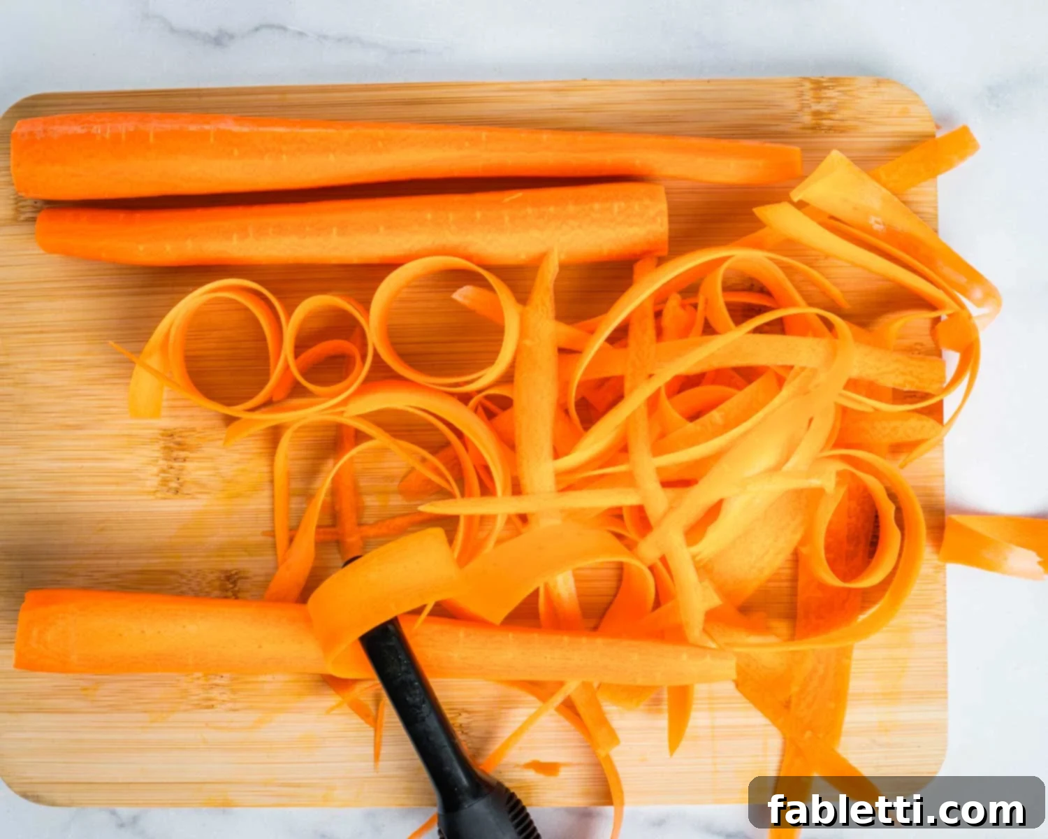 Sweet Heat Shaved Carrot Salad 4 A close-up shot of a cutting board, featuring large, fresh carrots and a hand skillfully using a vegetable peeler to create a long, thin ribbon of carrot.