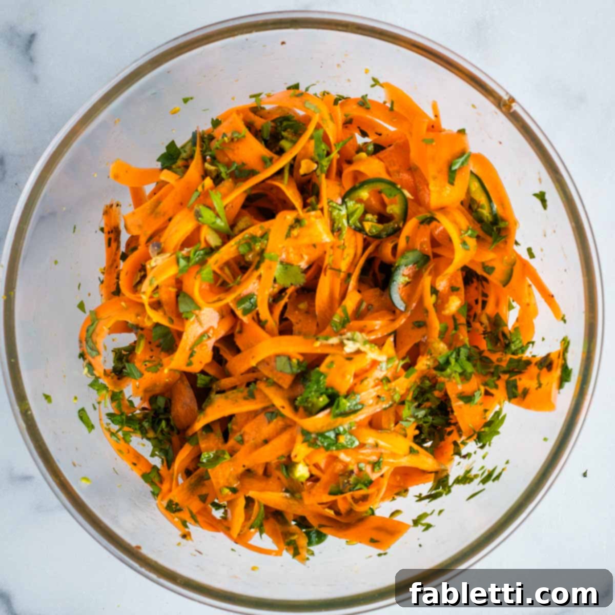 Sweet Heat Shaved Carrot Salad 9 A close-up shot of a pair of salad tongs actively mixing the colorful carrot ribbons, herbs, and other ingredients within a glass bowl, ensuring an even coating of the dressing.
