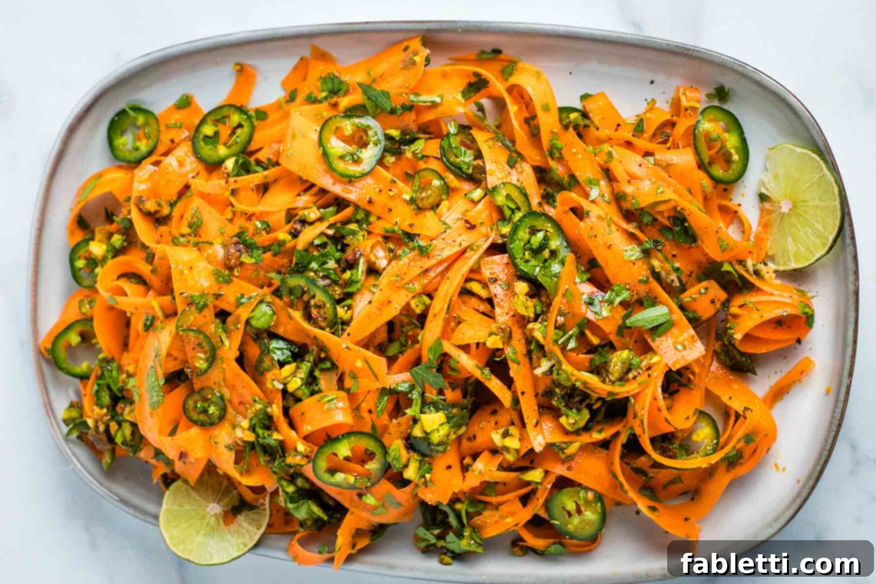 Sweet Heat Shaved Carrot Salad 10 A spread of vibrant carrot ribbons salad, served in a stylish bowl, surrounded by fresh ingredients like lime, jalapenos, and pistachios, ready to be enjoyed.