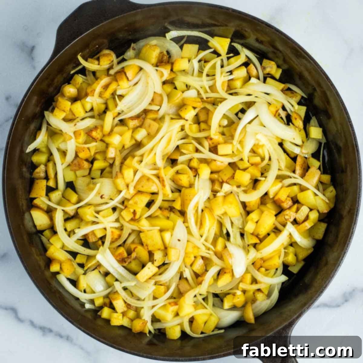 Simple Skillet Vegan Potato & Vegetable Hash 11 Thinly sliced onions being added to the browning potatoes in a hot skillet, ready to caramelize.