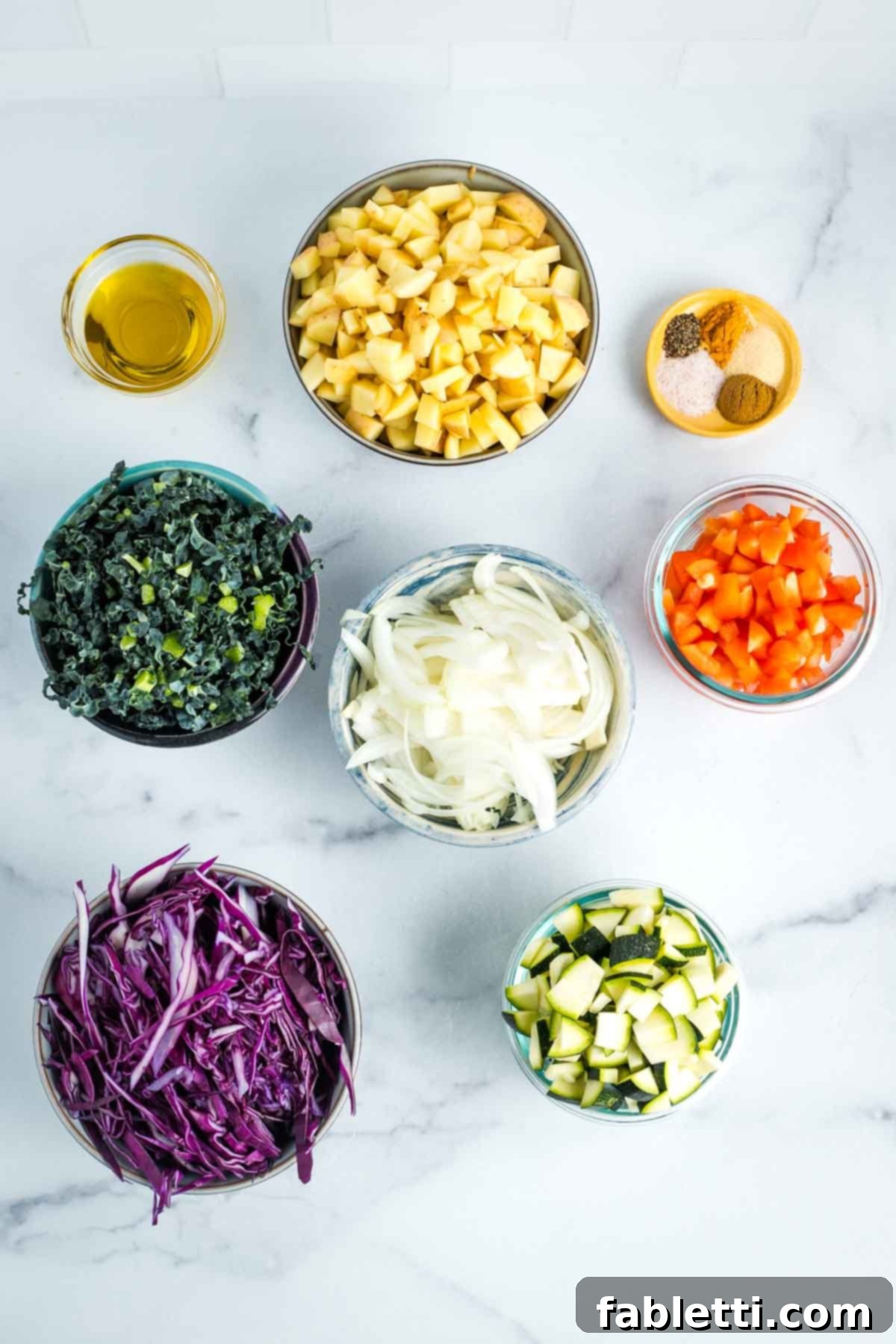 Simple Skillet Vegan Potato & Vegetable Hash 16 Arrangement of small bowls filled with meticulously chopped ingredients including potatoes, bell peppers, onion, cabbage, kale, and zucchini, alongside a small dish of olive oil and a variety of measured spices, all prepared for cooking.