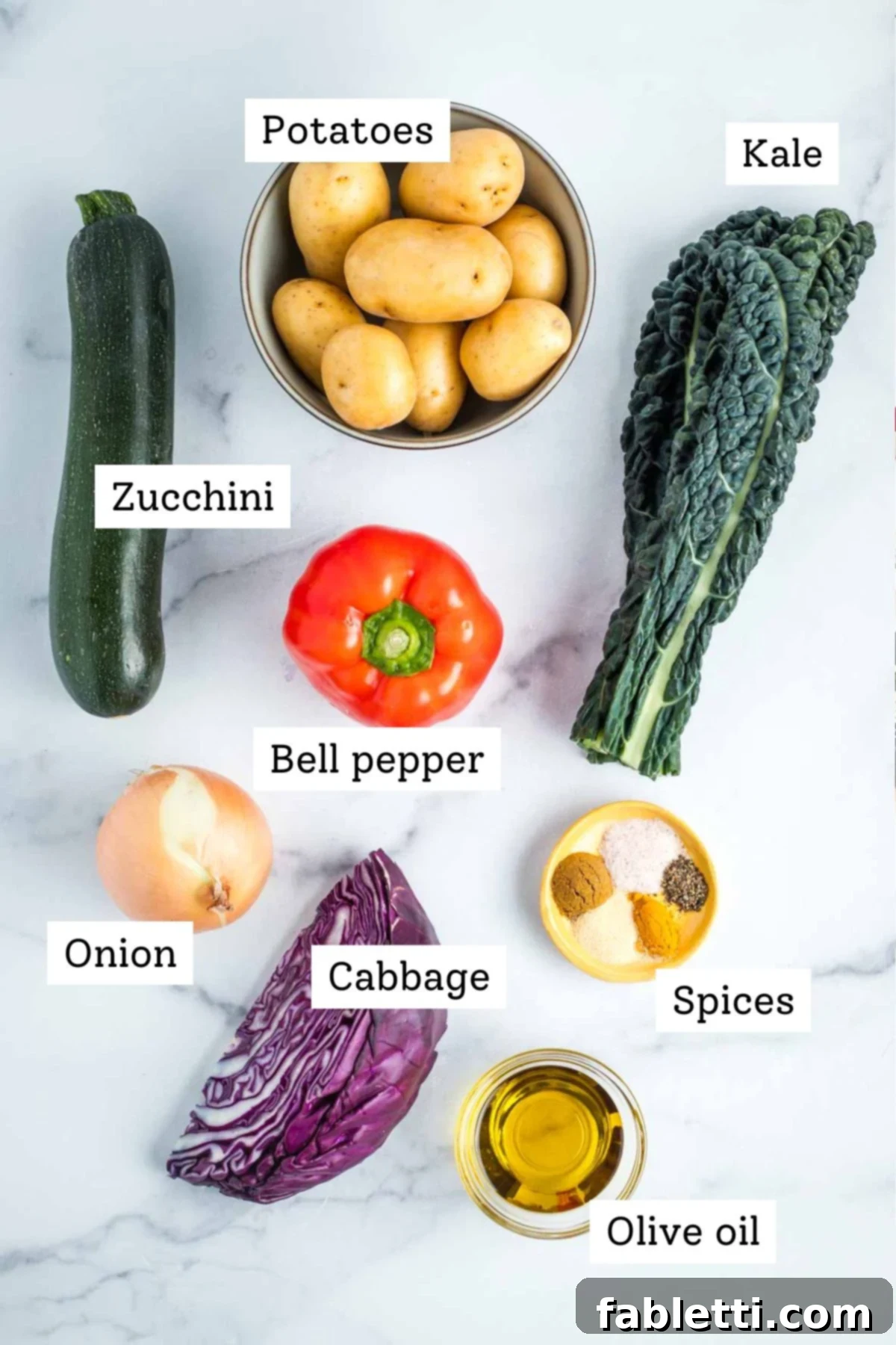 Simple Skillet Vegan Potato & Vegetable Hash 3 A selection of fresh, labeled ingredients for homemade veggie hash, including zucchini, diced potatoes, lacinato kale, red bell pepper, sliced onion, purple cabbage, and an array of Mediterranean spices with olive oil.