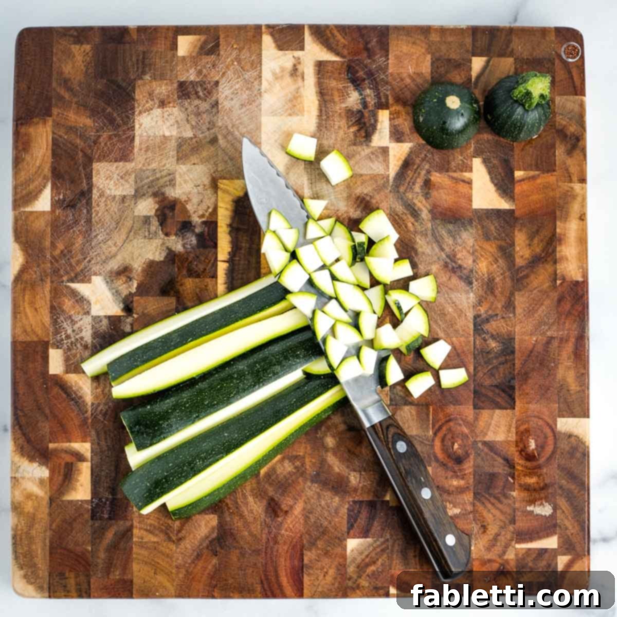 Simple Skillet Vegan Potato & Vegetable Hash 7 Clearly showing the process of dicing a fresh zucchini into small, even cubes on a wooden cutting board.