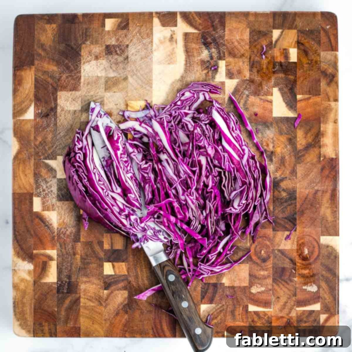 Simple Skillet Vegan Potato & Vegetable Hash 8 Demonstrating how to thinly slice a quarter of a vibrant purple cabbage on a wooden cutting board.