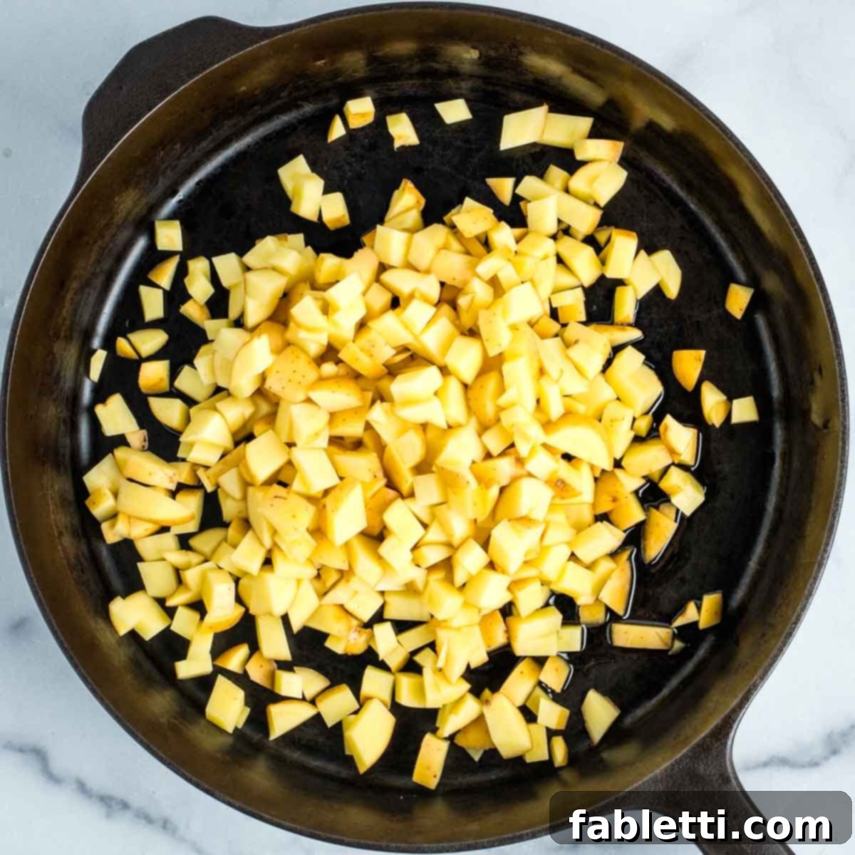 Simple Skillet Vegan Potato & Vegetable Hash 10 Diced potatoes being added to a hot skillet with olive oil, ready to be spread for initial browning.