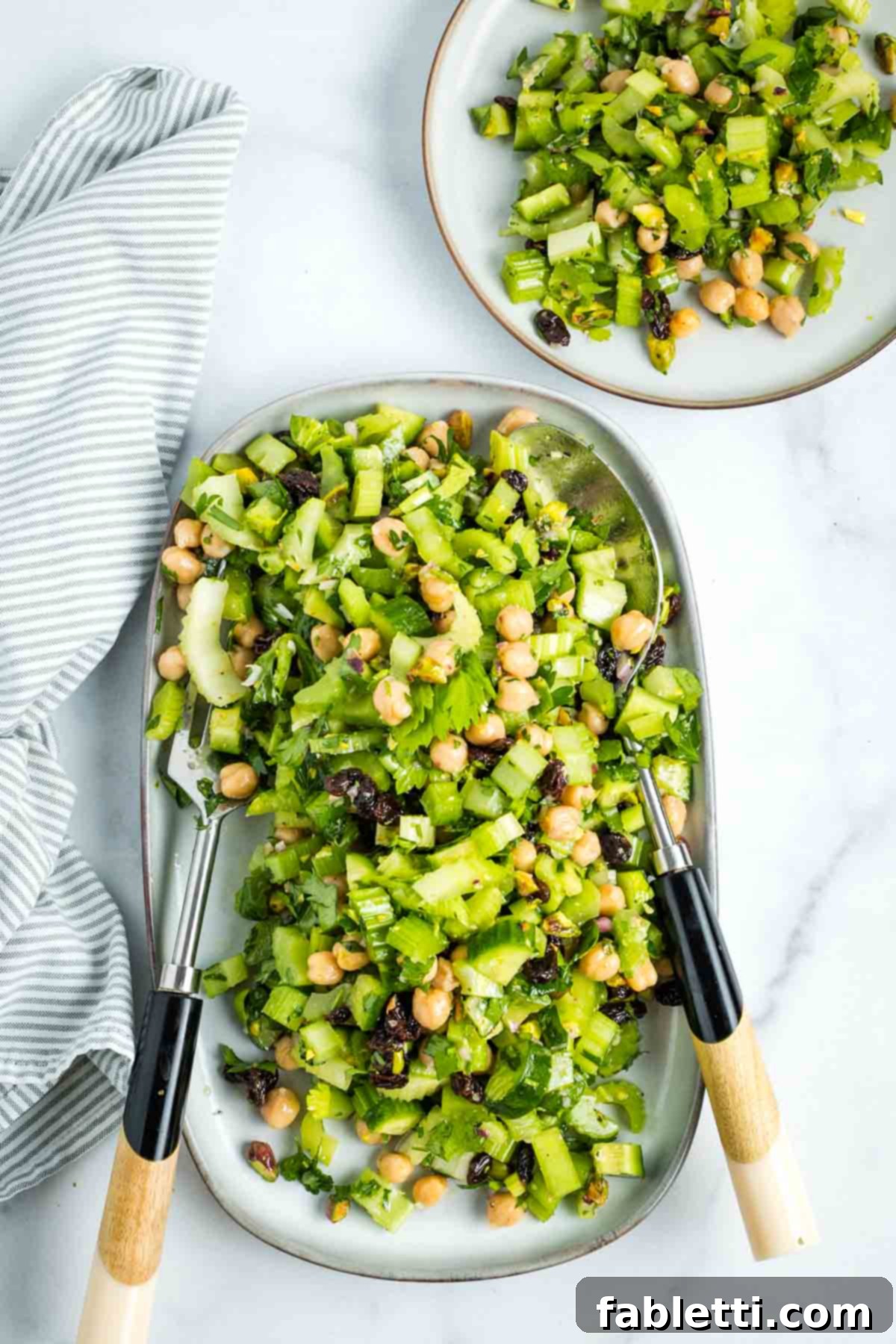 Crisp Celery & Chickpea Salad with a Sweet Raisin Twist 2 A vibrant chopped celery salad, featuring chickpeas, golden raisins, and green pistachios, perfectly portioned on a small white plate, ready to be enjoyed.