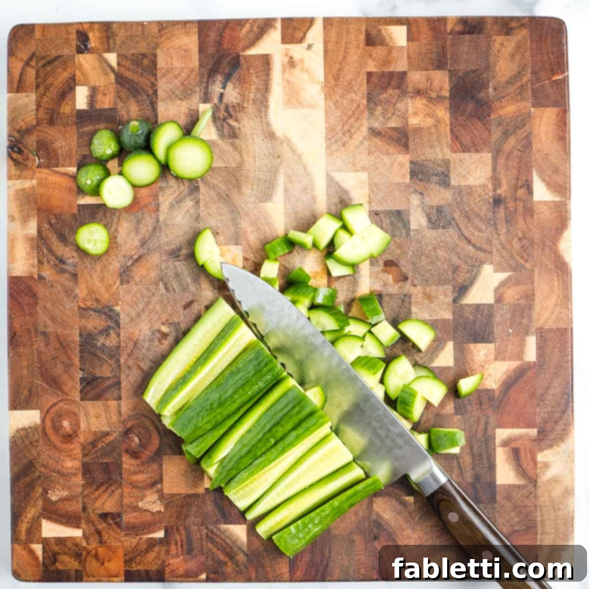 Crisp Celery & Chickpea Salad with a Sweet Raisin Twist 11 Cucumber strips are precisely cut across into small, uniform dice on a wooden cutting board, ensuring even pieces for a chopped salad.