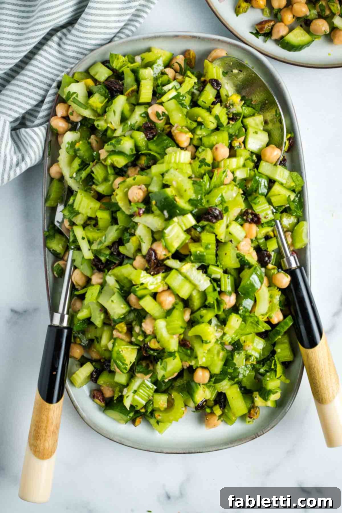 Crisp Celery & Chickpea Salad with a Sweet Raisin Twist 15 A beautifully presented serving of chopped celery salad, garnished with raisins, pistachios, fresh parsley, and chickpeas, highlighting its fresh and wholesome ingredients.
