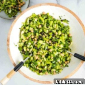 Crisp Celery & Chickpea Salad with a Sweet Raisin Twist 16 A close-up of a refreshing chopped celery salad, vibrant with chickpeas, golden raisins, delicate shallots, crisp cucumber, crunchy pistachios, and fresh herbs, ready to be served.