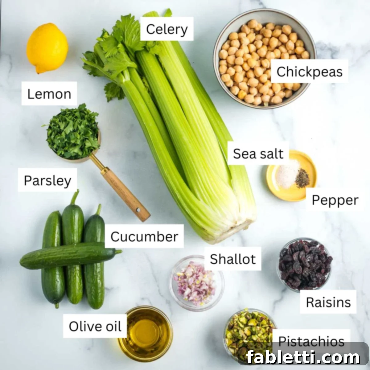 Crisp Celery & Chickpea Salad with a Sweet Raisin Twist 3 A beautiful flat lay of fresh salad ingredients: vibrant lemon, wholesome chickpeas, crisp celery, aromatic parsley, cool cucumber, rich olive oil, delicate shallot, crunchy pistachios, and sweet raisins, all ready for chopping.