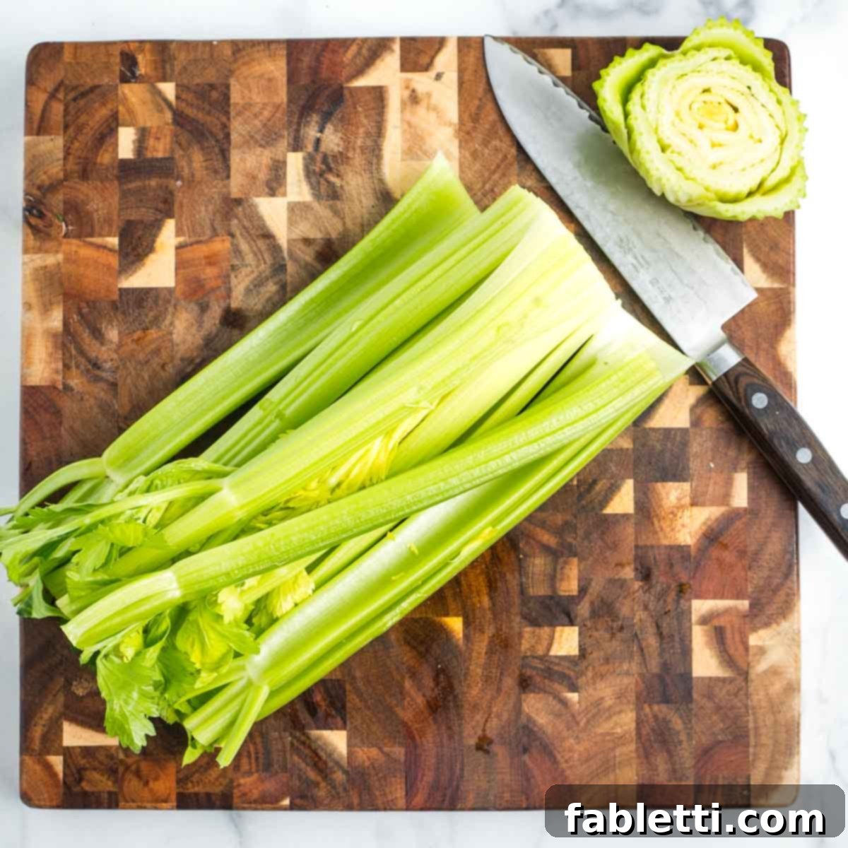 Crisp Celery & Chickpea Salad with a Sweet Raisin Twist 4 The root end of a celery head has been cleanly cut off, revealing fresh stalks, resting on a rustic wooden cutting board.