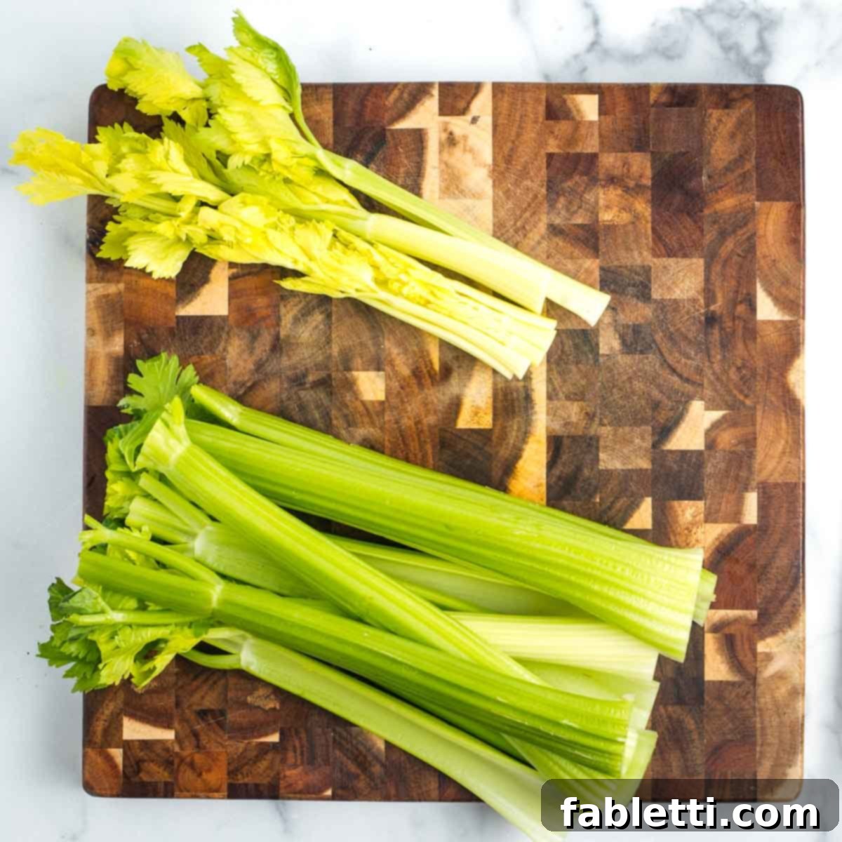 Crisp Celery & Chickpea Salad with a Sweet Raisin Twist 5 Two distinct piles of celery stalks on a wooden board: one features the darker, firm outer stalks, while the other holds the lighter, flimsier inner stalks with leaves.