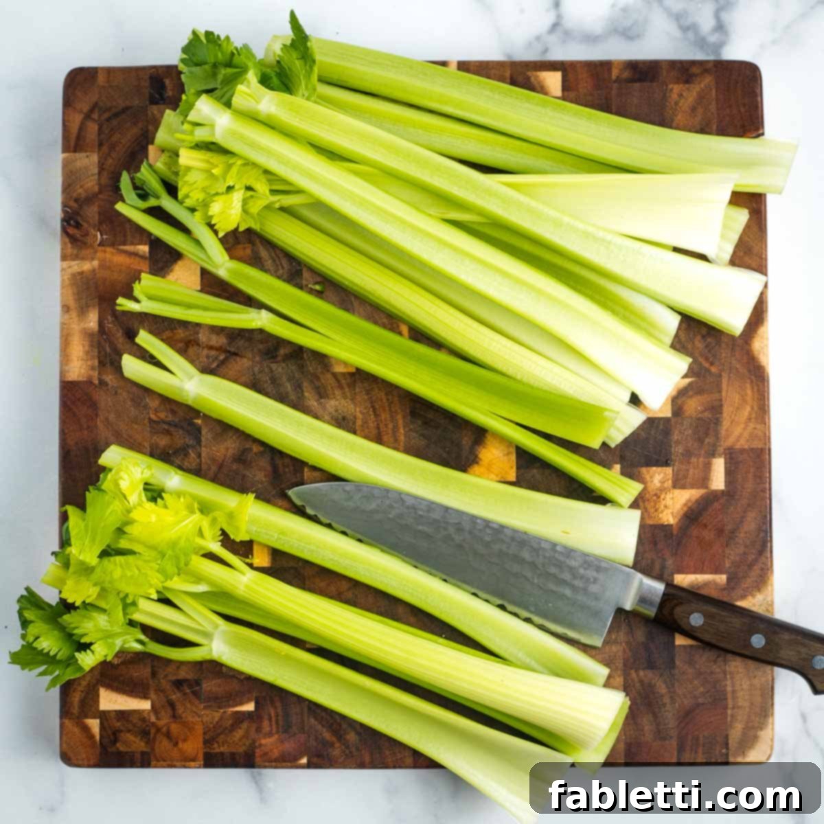 Crisp Celery & Chickpea Salad with a Sweet Raisin Twist 6 A chef's knife precisely cuts wide celery stalks in half lengthwise on a wooden cutting board, preparing them for dicing.