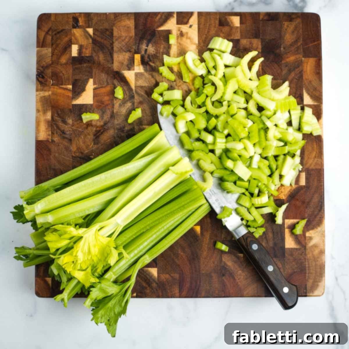 Crisp Celery & Chickpea Salad with a Sweet Raisin Twist 7 Halved celery stalks are expertly sliced across into small, even diced pieces on a wooden cutting board, ideal for a chopped salad.
