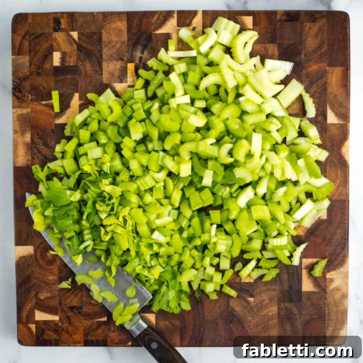 Crisp Celery & Chickpea Salad with a Sweet Raisin Twist 8 A wooden cutting board is completely covered with a mound of freshly chopped, vibrant green celery, ready for the salad bowl.