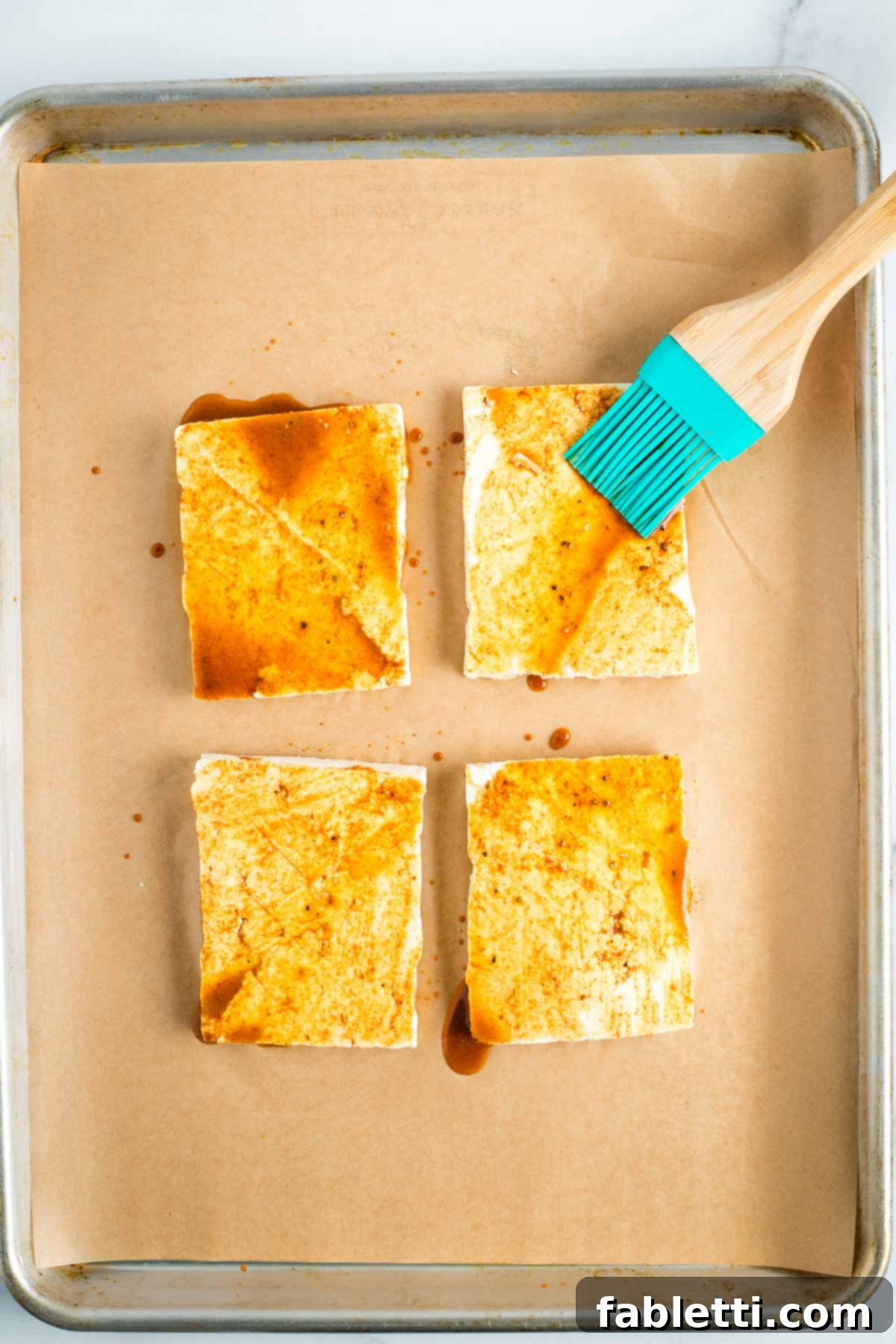 Brushing marinade onto tofu steaks on a sheet pan.