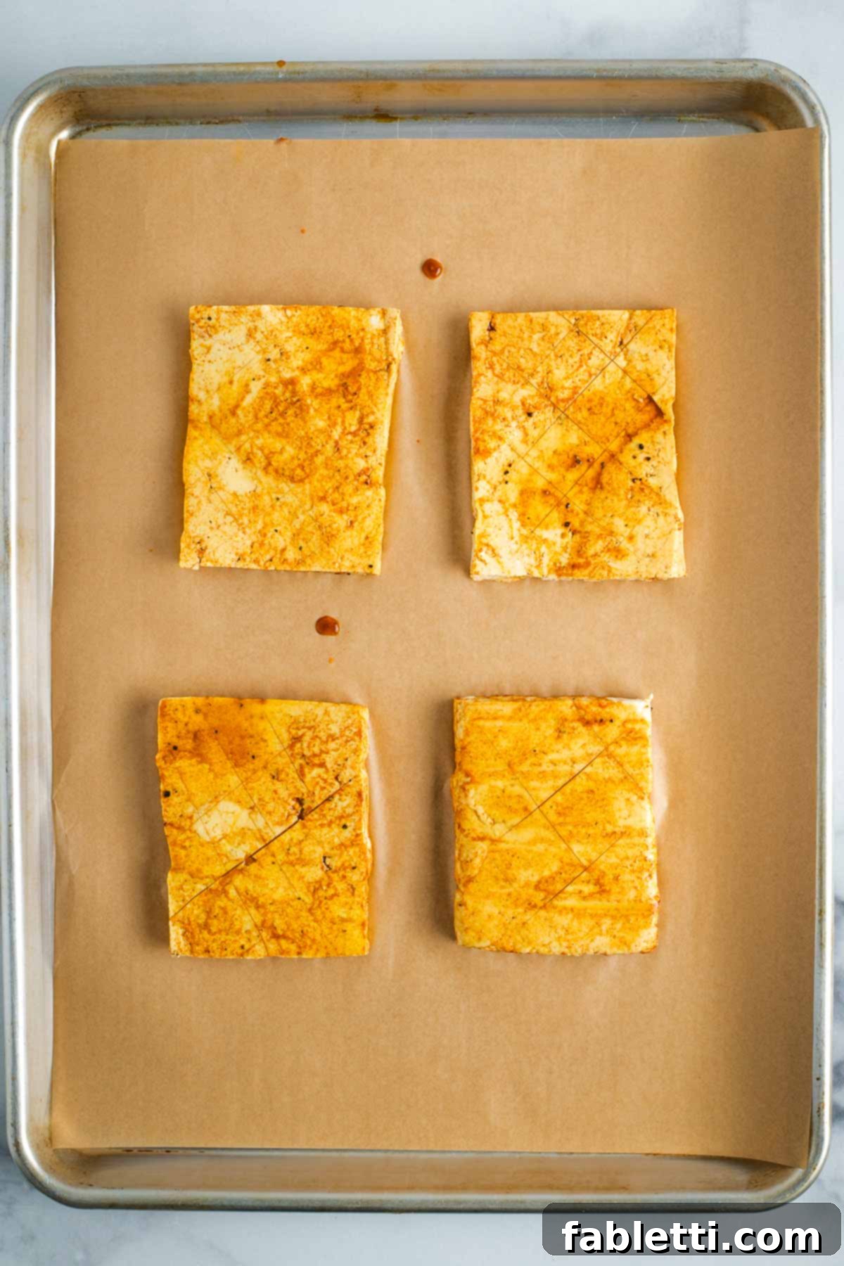 Scored tofu steaks on a sheet pan with brown sauce.