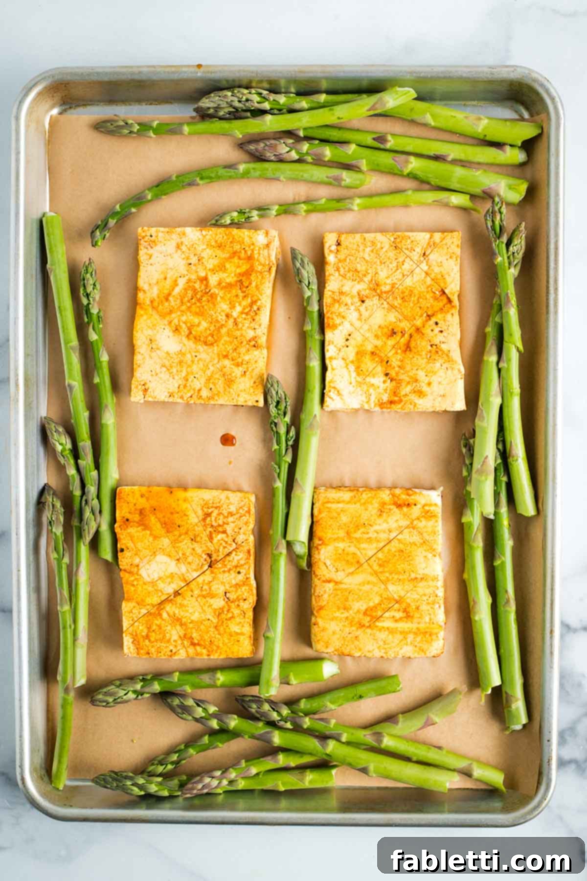 Marinated tofu steaks on a sheet pan surrounded by asparagus.