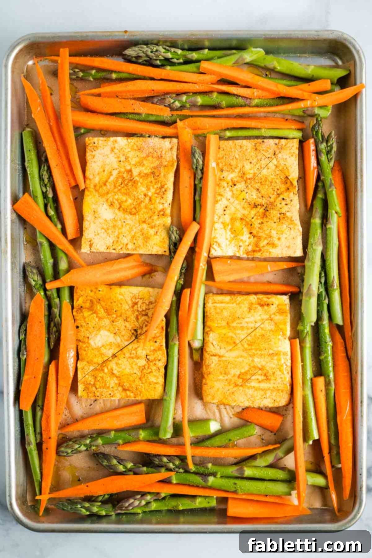 Marinated tofu steaks surrounded by carrots and asparagus on a sheet pan.