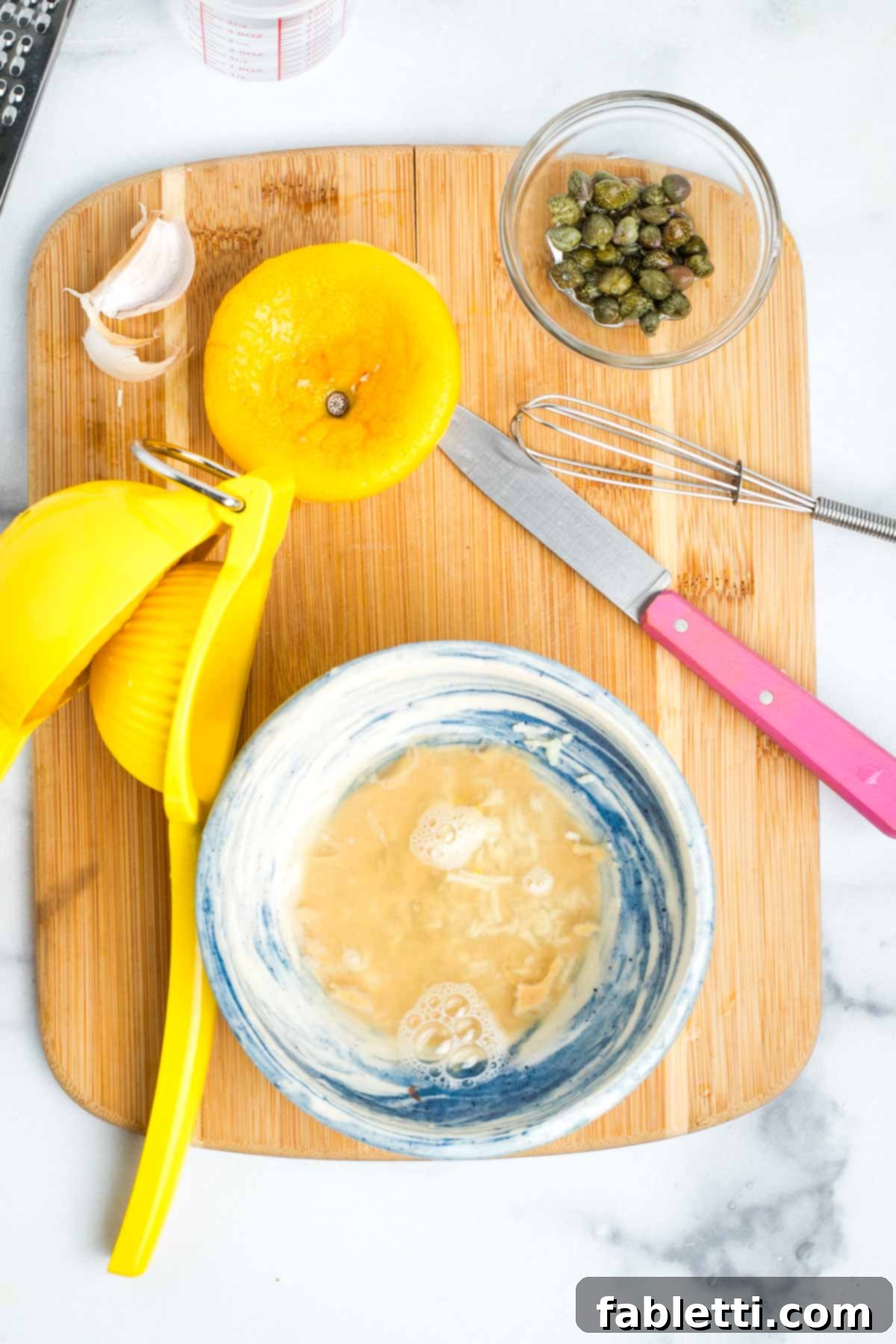 Small bowl with tahini and lemon juice on a cutting board with a dish of capers.