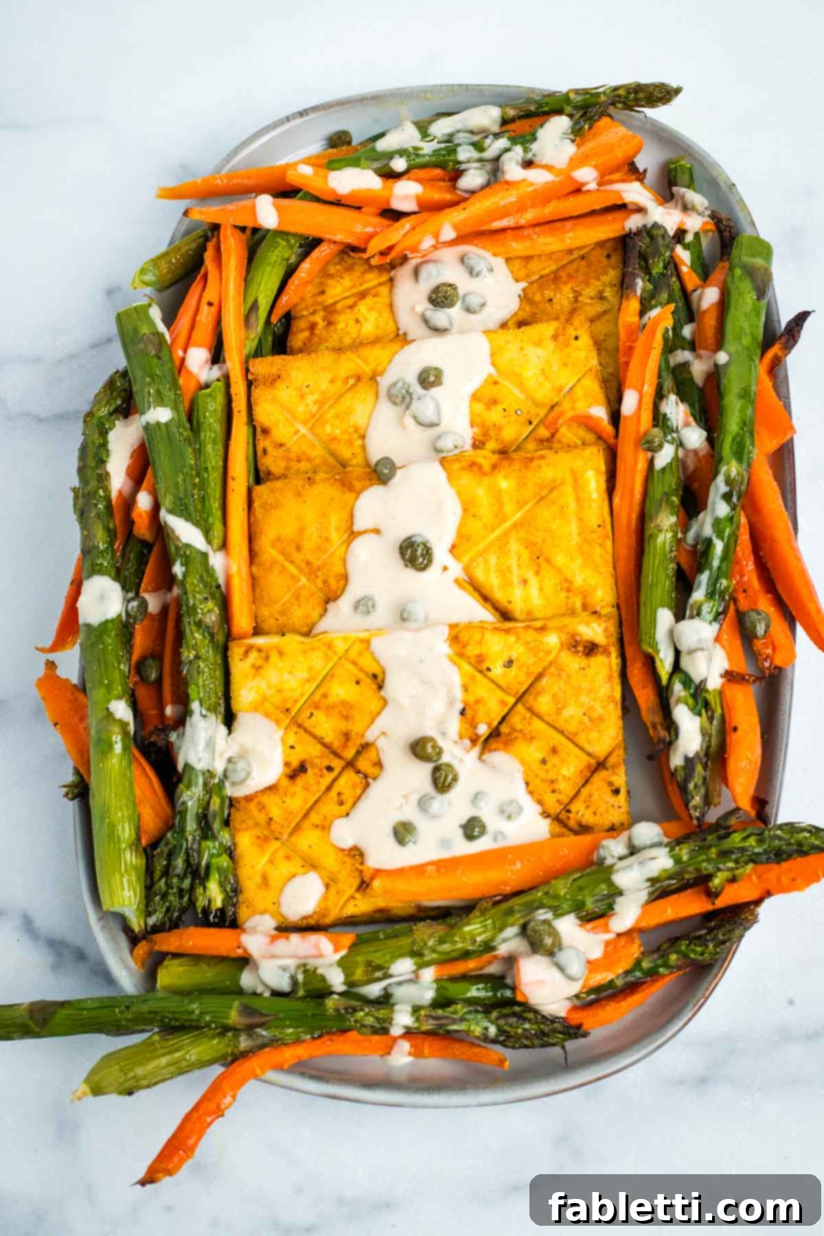 Tofu steaks and roasted carrots and asparagus, drizzled with creamy caper sauce on a platter.