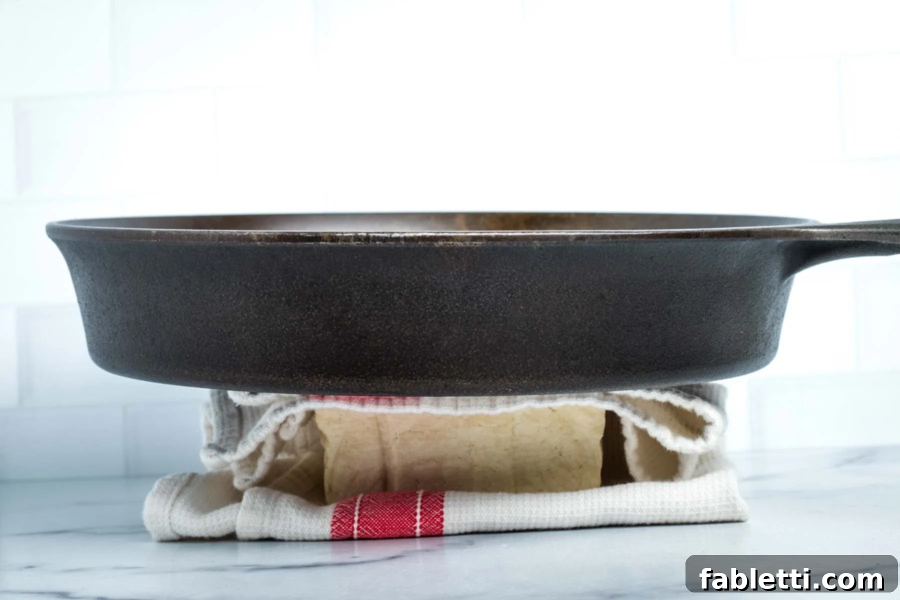 Cast iron skillet sitting on top of a block of tofu in a dish towel.