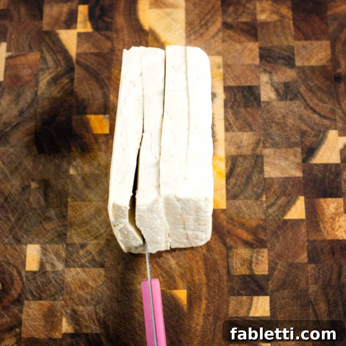 A block of tofu being cut into 4 steak slabs.