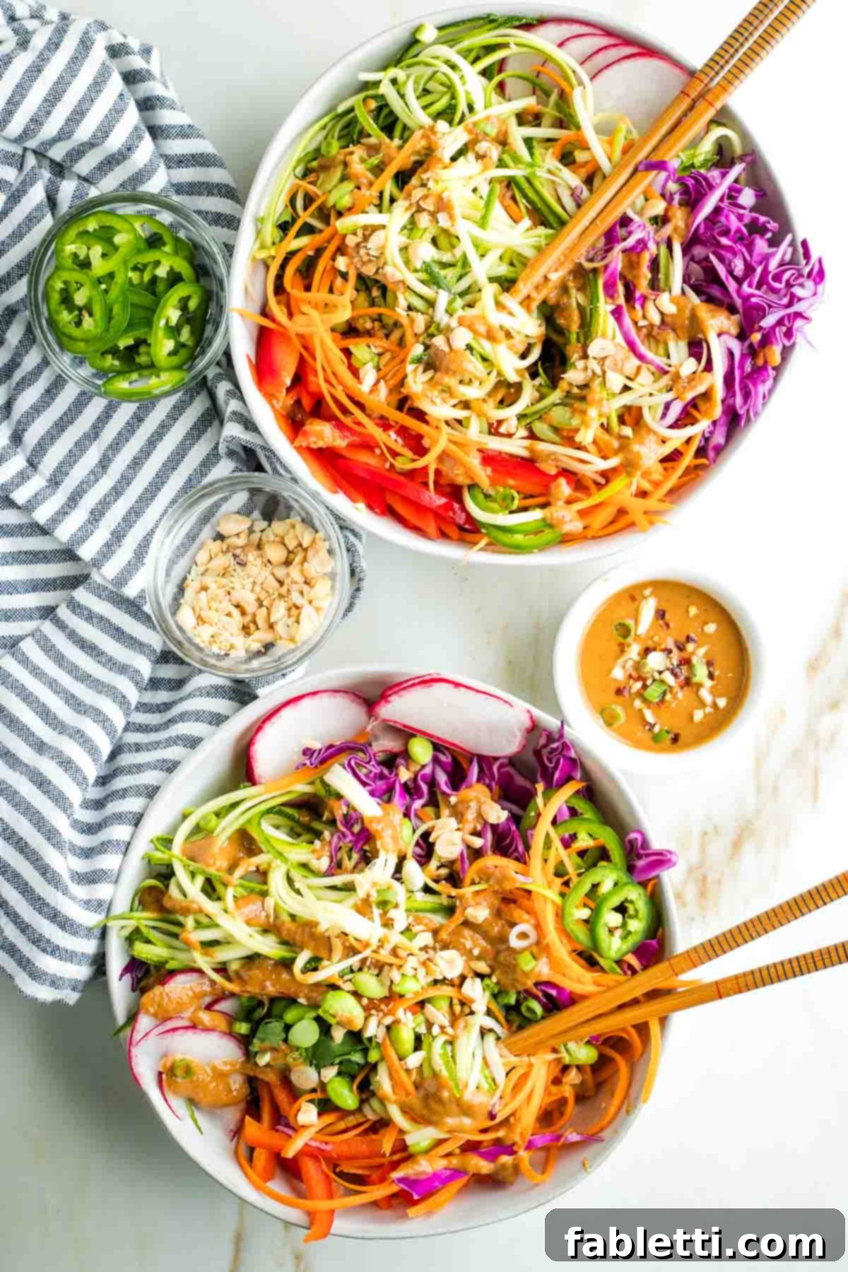 Fresh Spring Roll Salad Bowl with Creamy Peanut Sauce 2 Noodles made from zucchini and carrots, twirled onto chopsticks, covered in peanut sauce with more colorful veggies in the bowl, sprinkled with peanuts and jalapenos.