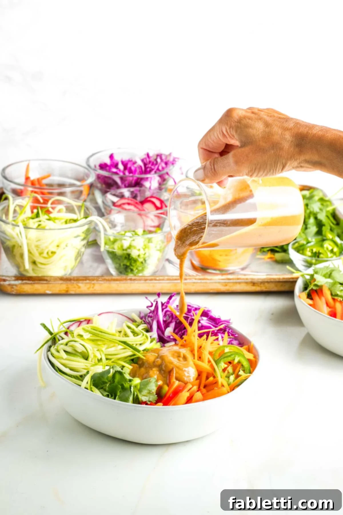 Fresh Spring Roll Salad Bowl with Creamy Peanut Sauce 17 Pouring peanut sauce onto a bowl full of brightly colored veggies for a spring roll bowl.