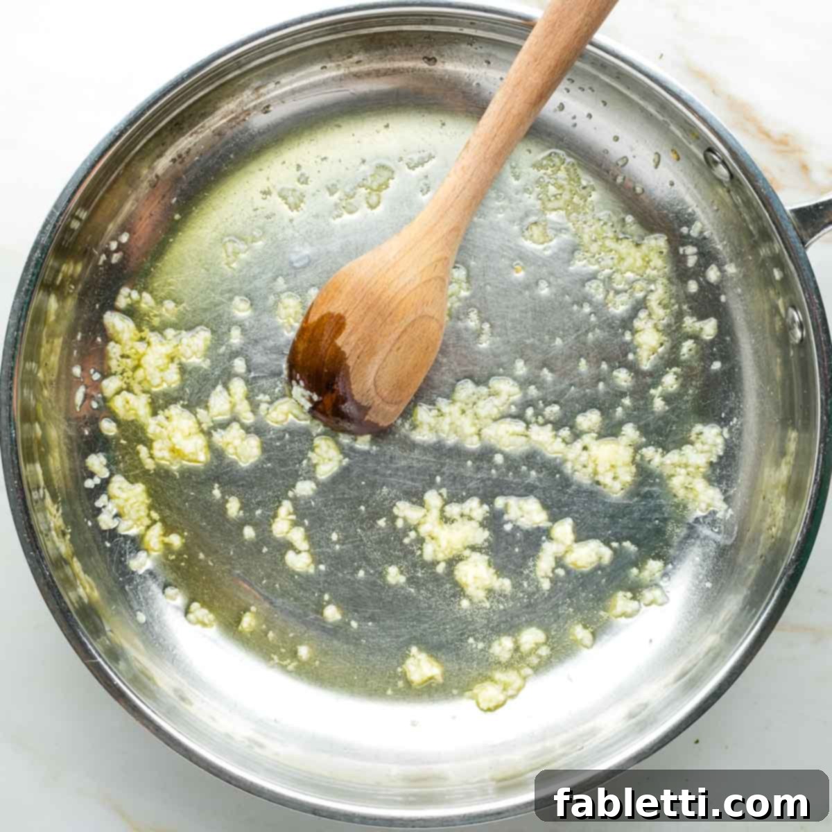 Zesty White Bean Puttanesca Pasta 5 Crushed garlic gently cooking in olive oil, stirred with a wooden spoon in a skillet.