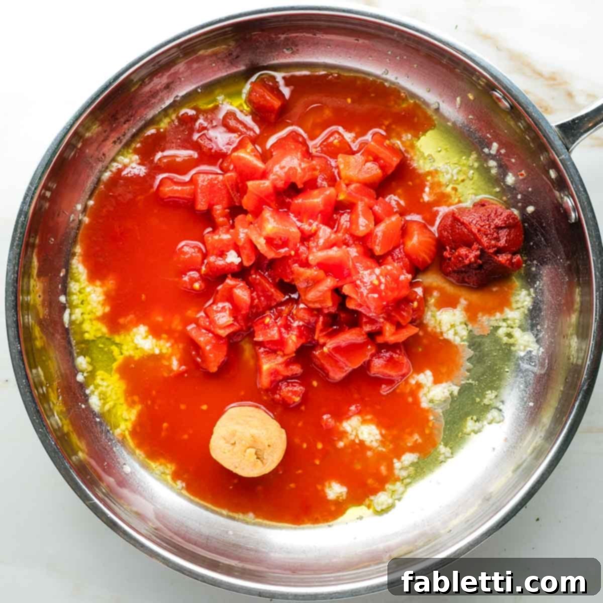 Zesty White Bean Puttanesca Pasta 6 Diced tomatoes, tomato paste, and miso paste being combined with garlic and olive oil in a skillet.
