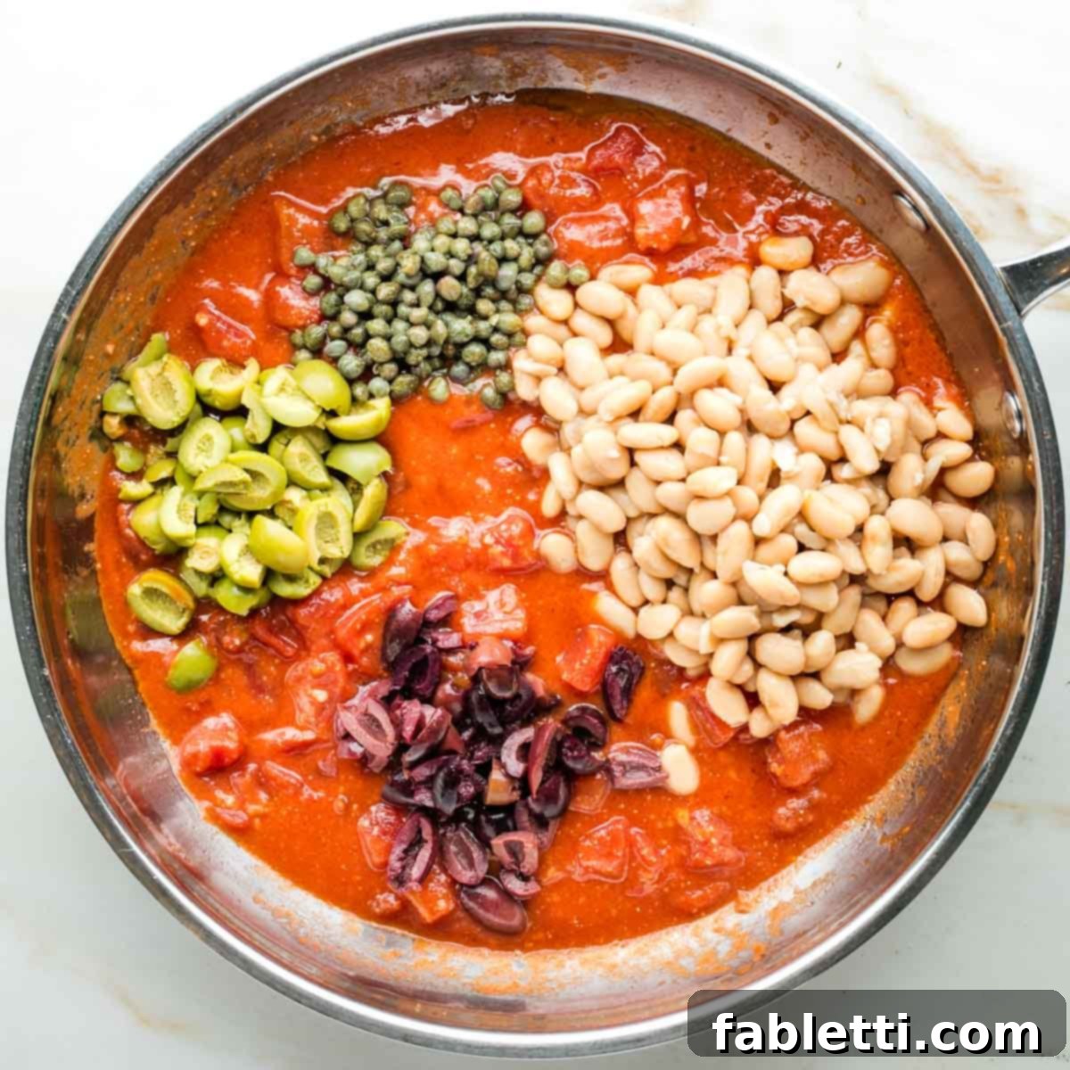 Zesty White Bean Puttanesca Pasta 7 Saucy diced tomatoes with roughly chopped olives, capers, and rinsed white beans in a skillet.